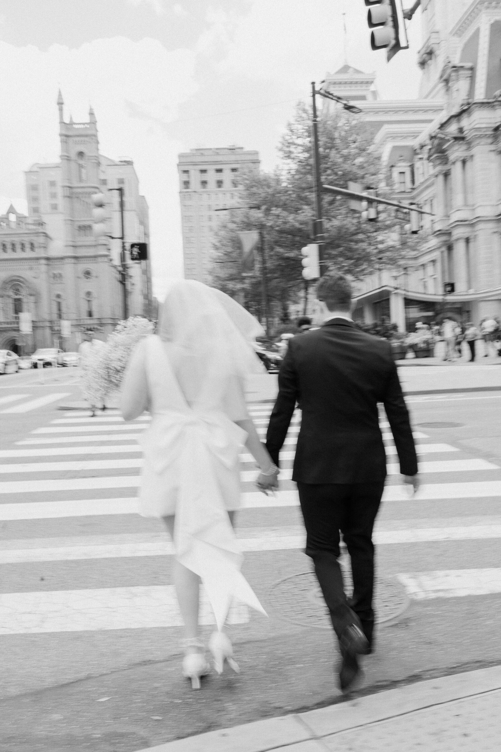 black and white motion blur image of bride and groom holding hands and walking across a cross walk, away from camera