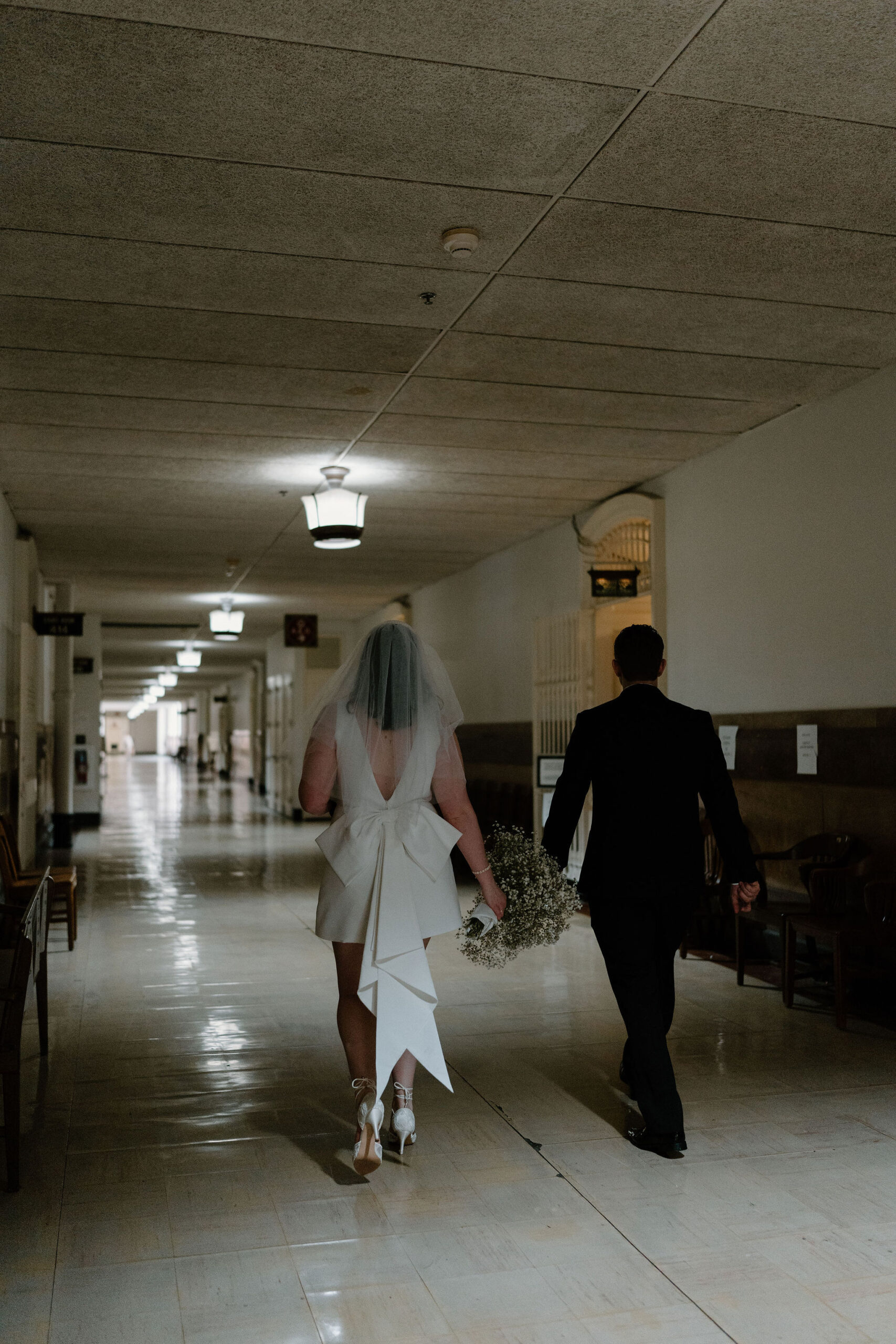 bride and groom walking down a dimly lit hallway to turn in their marriage license