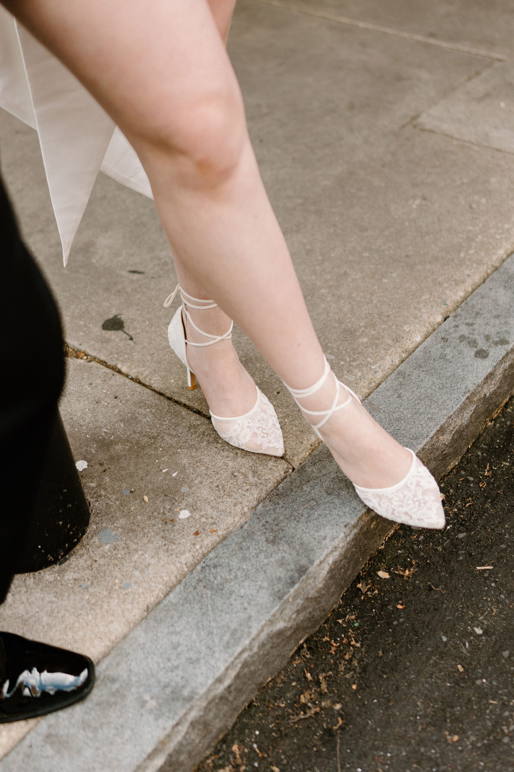 close up of bride's lacy wedding heels standing on a concrete curb