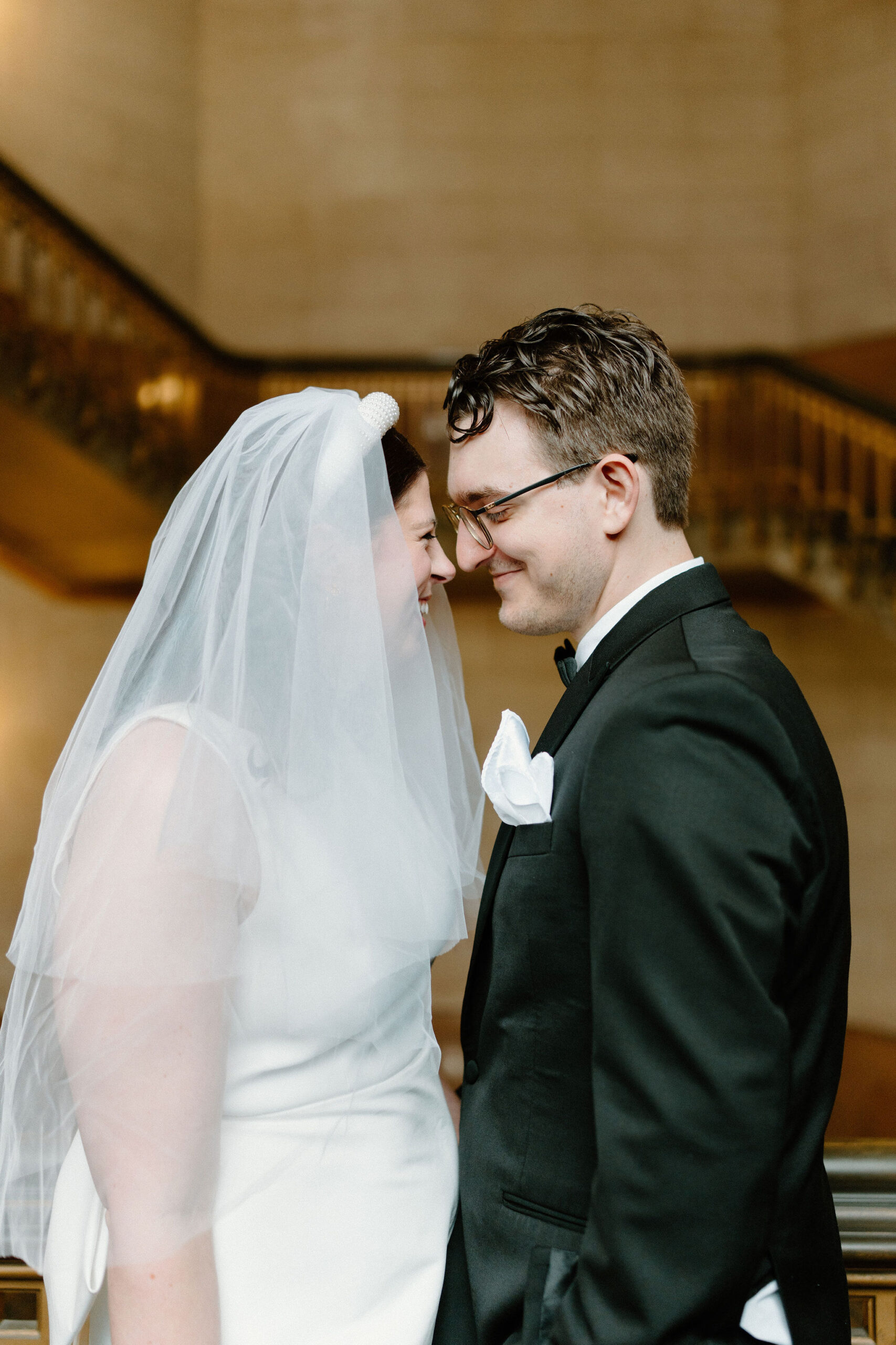 close up of bride and groom in large stairwell, leaning noses together and smiling at each other