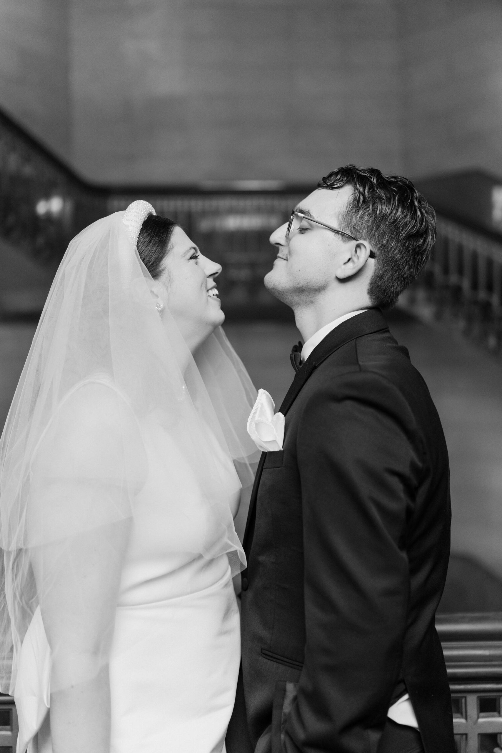 black and white close up of bride and groom smiling at each other, inside large winding stairwell