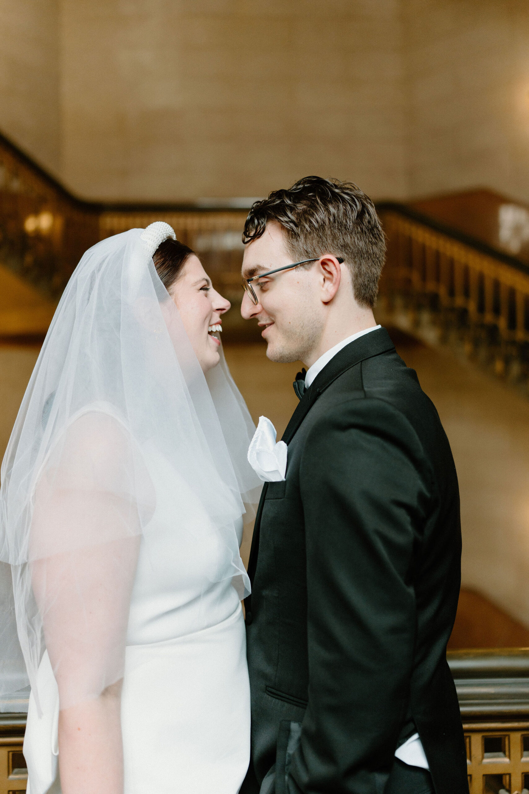 close up of bride and groom in large stairwell, talking and laughing toward each other