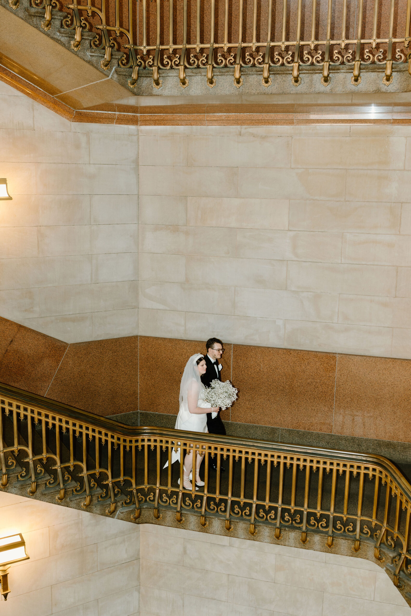 wide image of bride and groom holding hands and walking together down a large spiral staircase