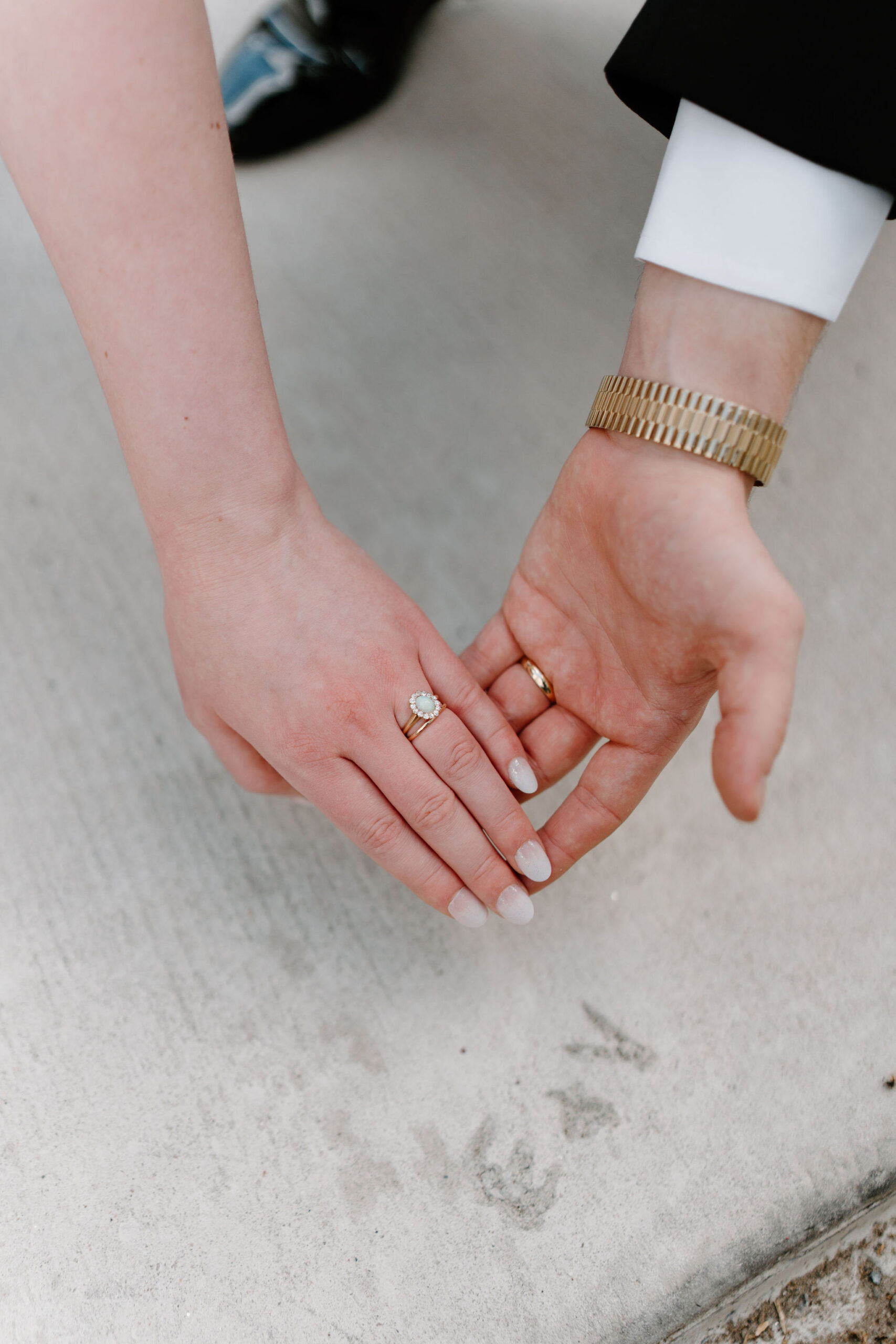 bride and groom's hands, sporting their new wedding bands, over sidewalk carving of "E+V"