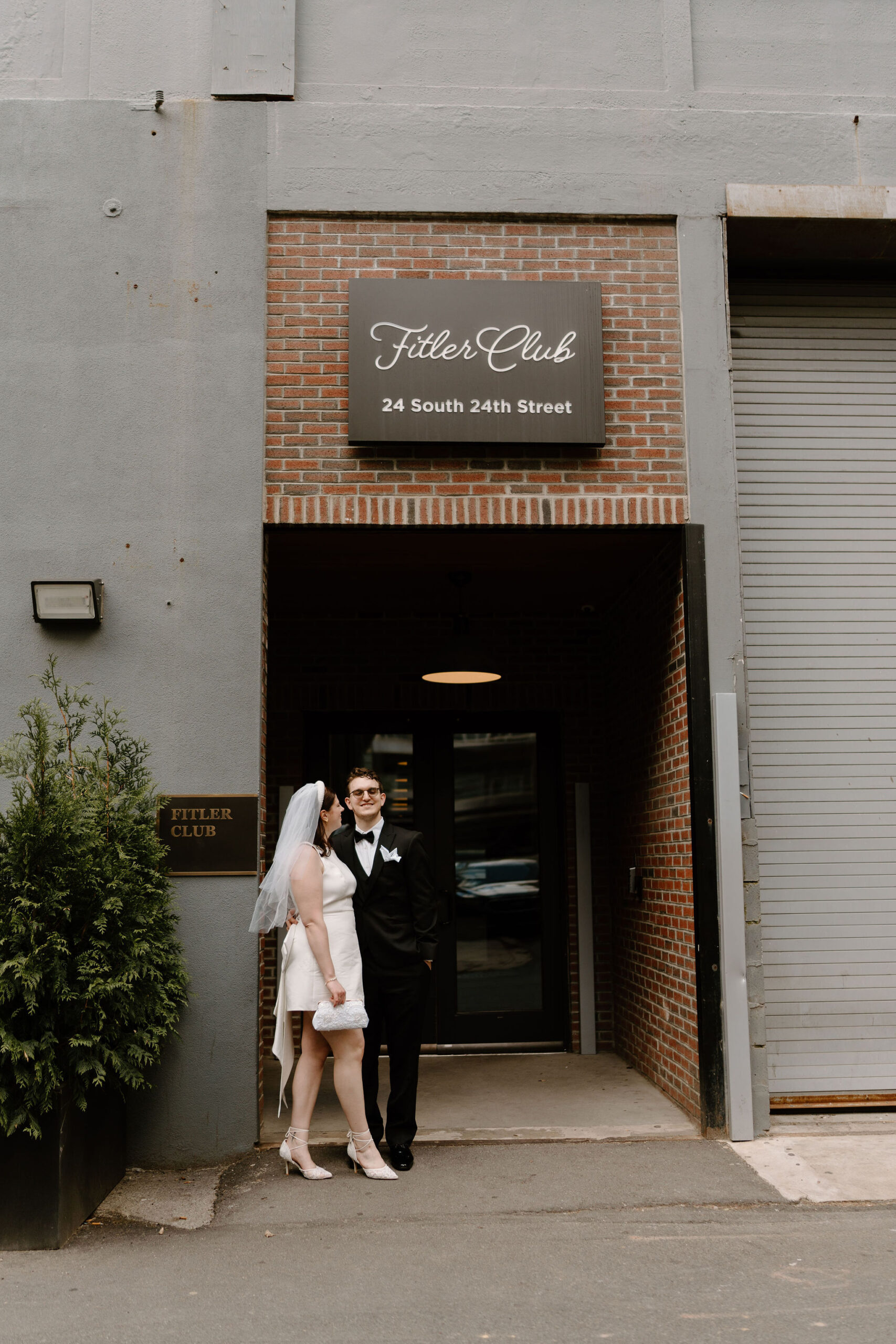 bride and groom in front of the venue of their private lunch, the Fitler Club, groom smiling at the camera and bride smiling at him