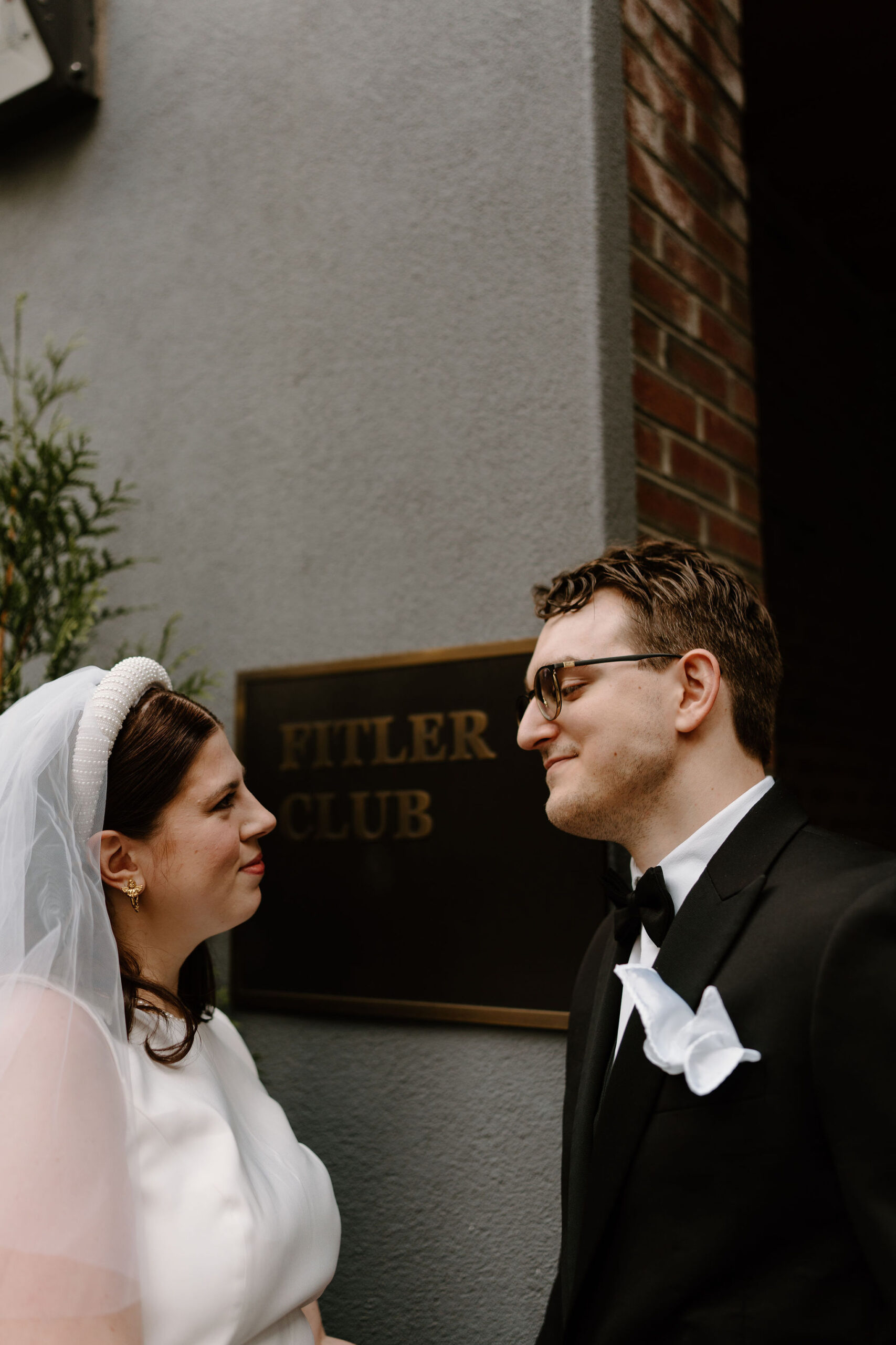 bride and groom smiling softly at each other, in front of a sign that read "Fitler Club"