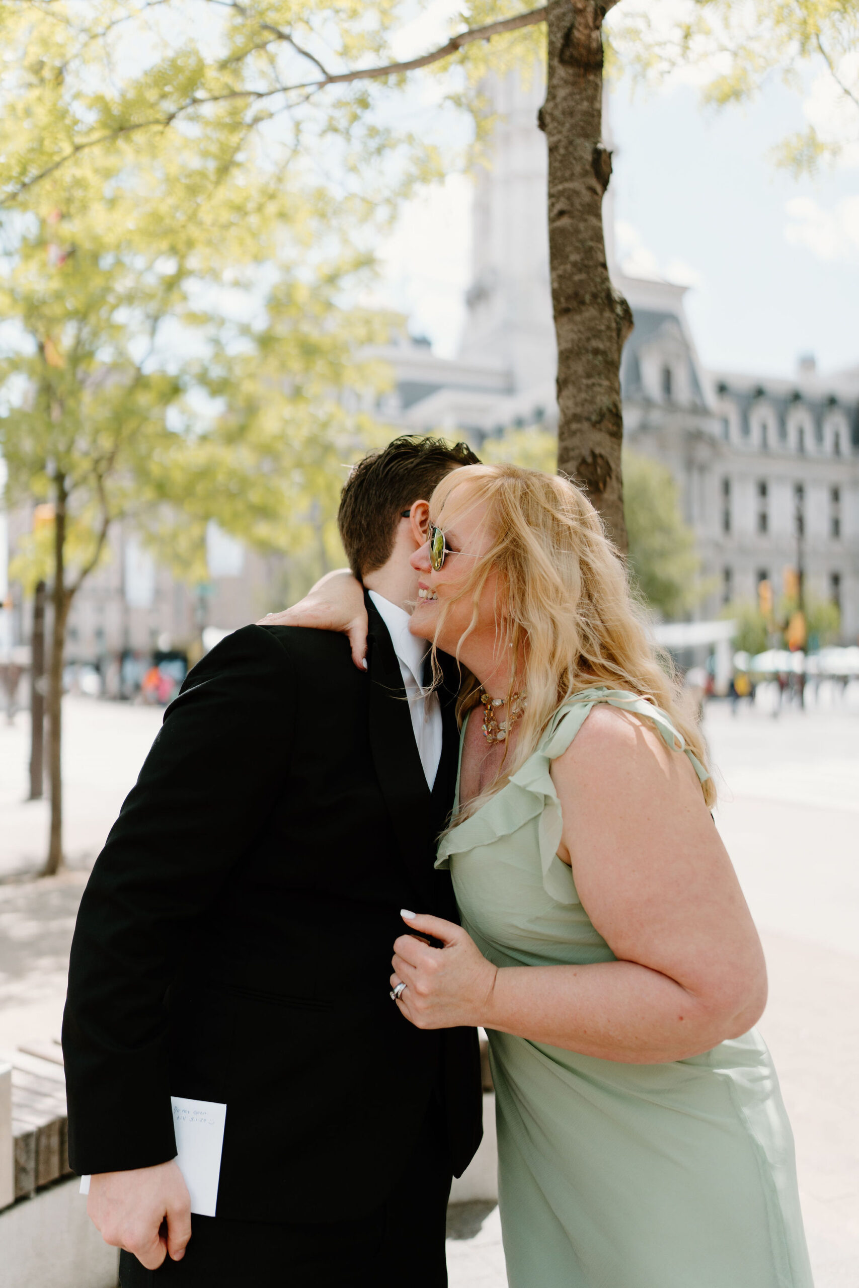 bride's mother (blonde hair, green dress) hugging groom (black suit, glasses) 