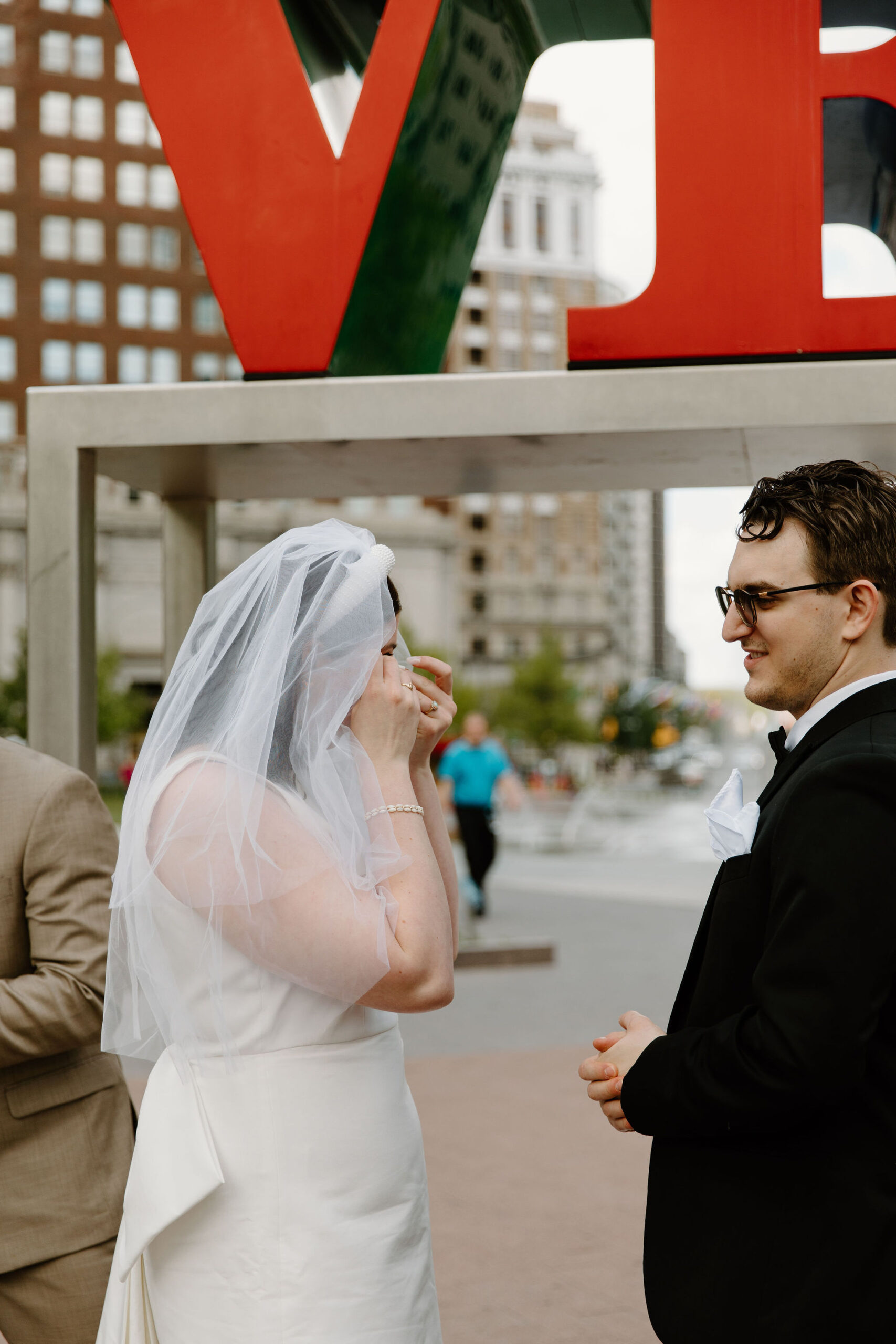 bride crying and dabbing her eyes with a tissue during wedding ceremony, while groom stands next to her