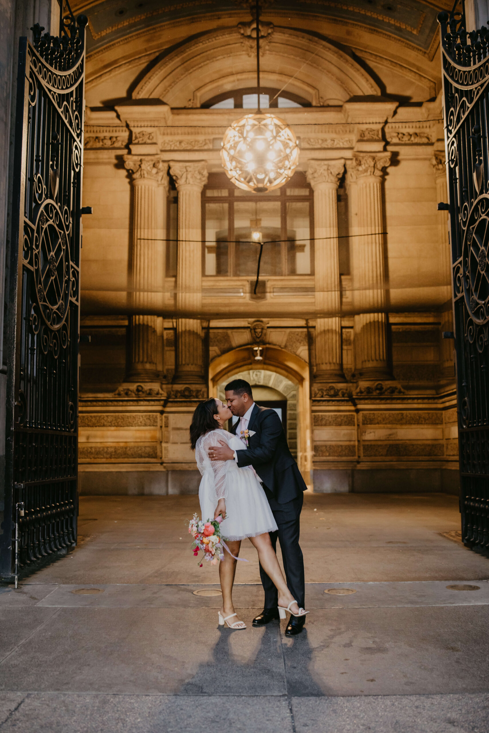 groom dipping a bride in a short white wedding dress at the open gates of City Hall in Philadelphia