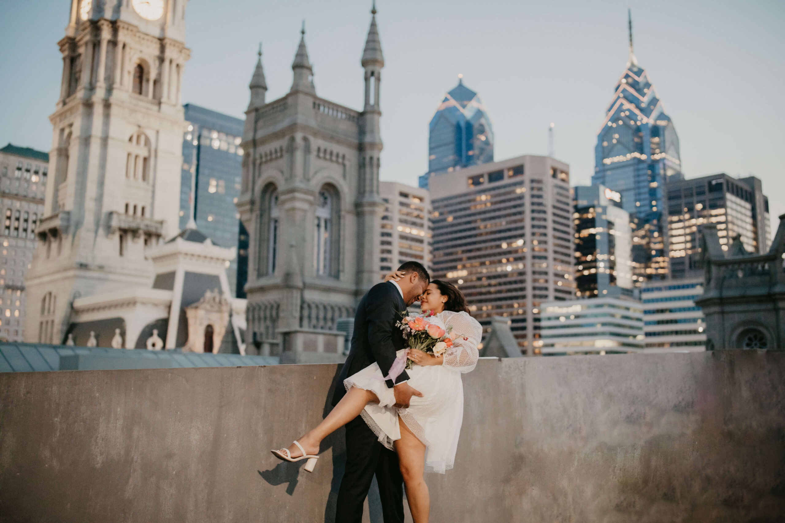 bride being dipped by her groom on top of a parking garage in center city Philadelphia, with the city skyline lit up behind them
