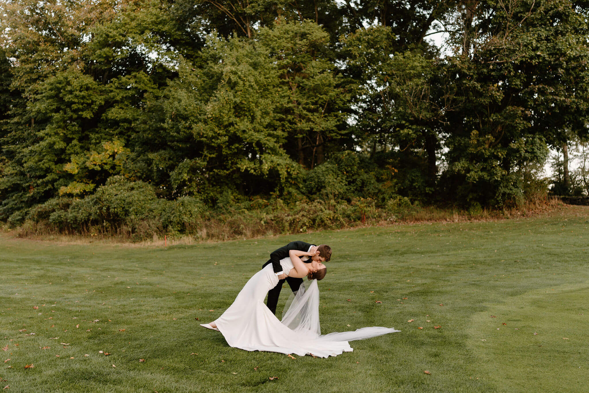 groom dipping bride during golden hour, trees behind them, while her veil and the train of her gown flow out behind her