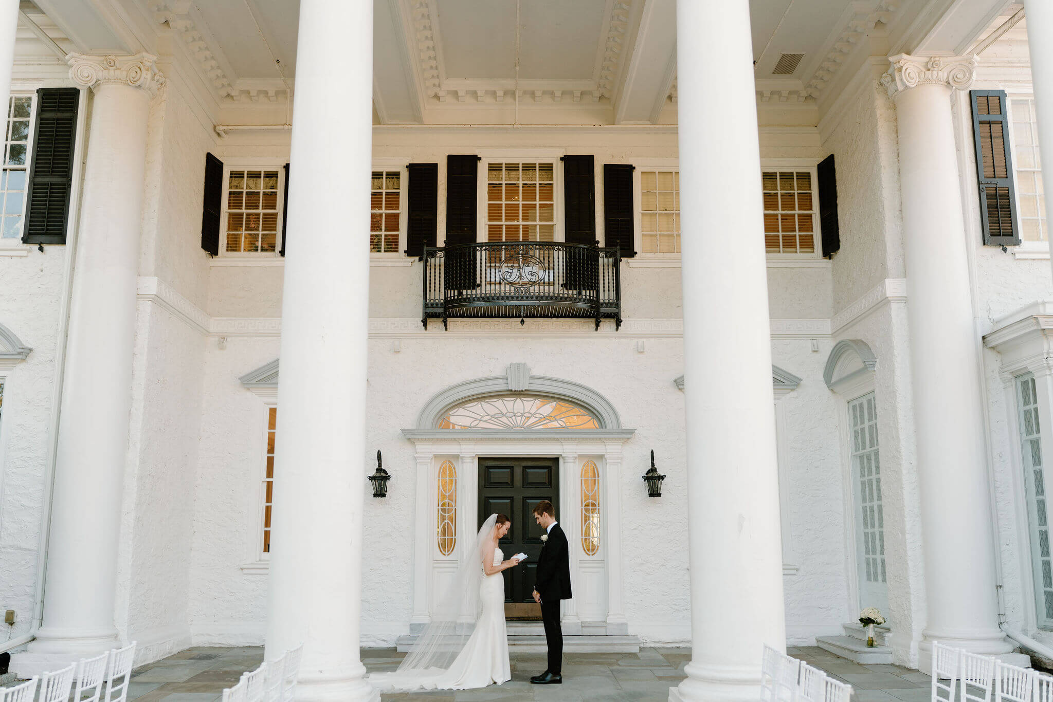 bride (white open back wedding gown, cathedral length veil) and groom (black suit) exchanging wedding vows privately in front of the Radnor Valley Country Club clubhouse