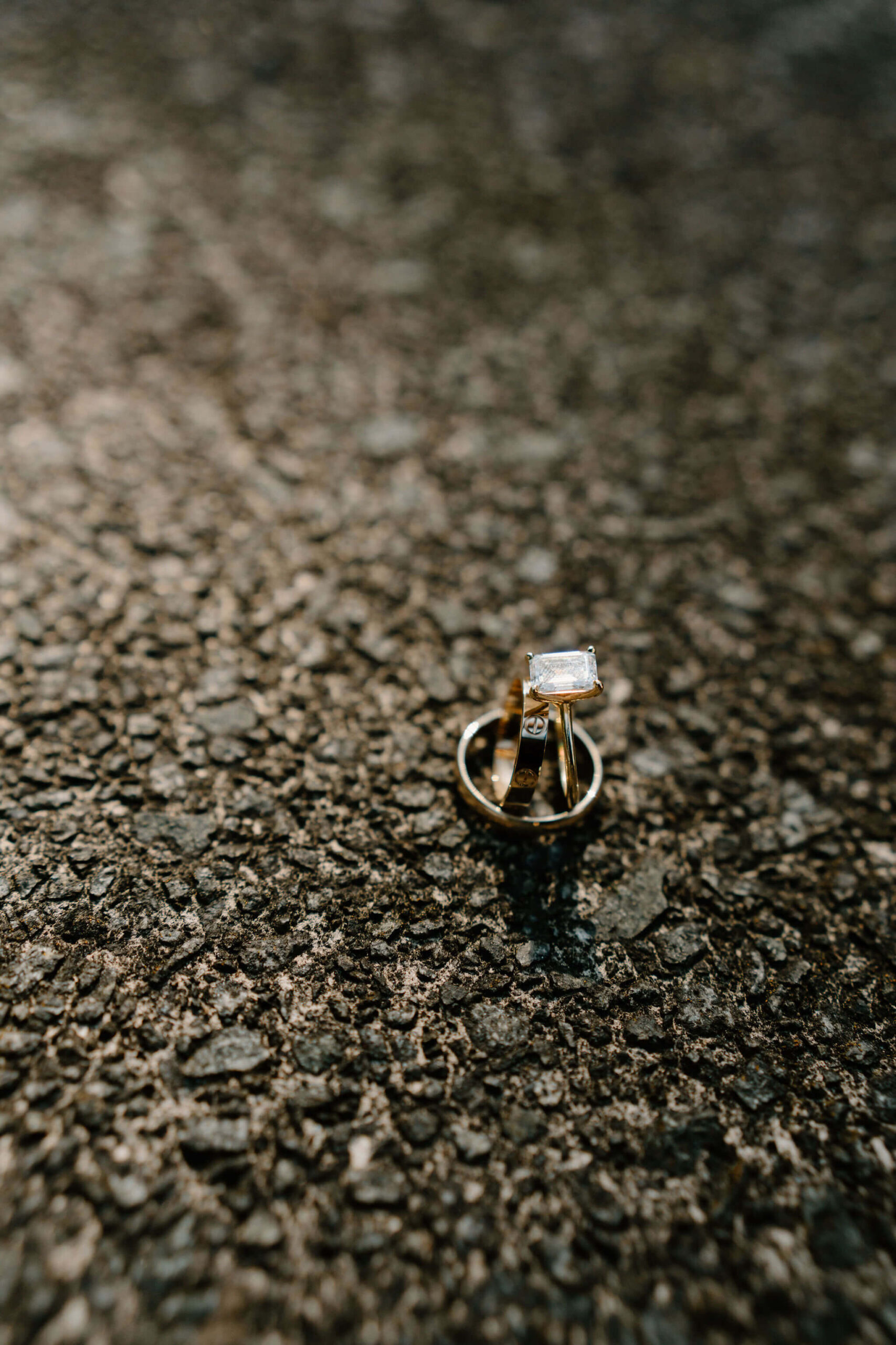 close up of a gold emerald cut engagement ring, and two gold wedding bands leaning together