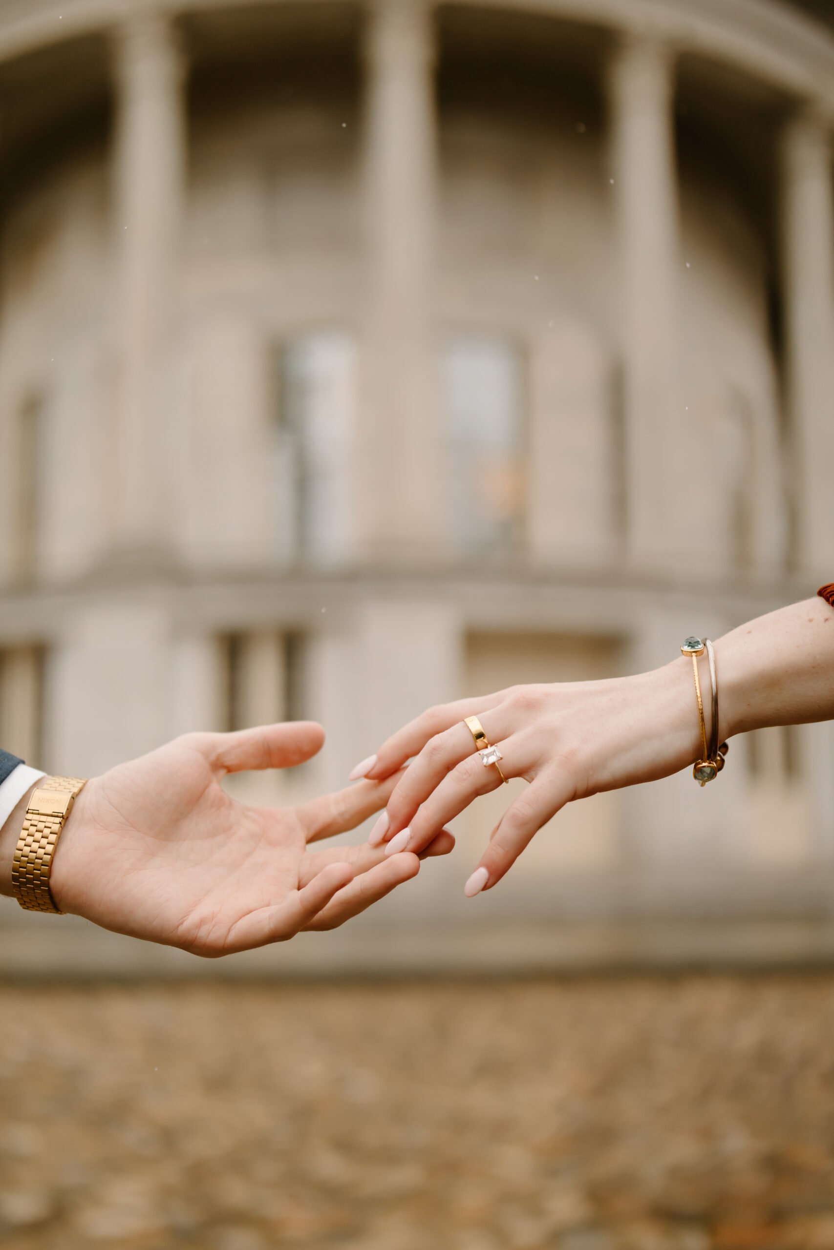 engaged couples' hands reaching toward each other, focused on her engagement ring, in front of the Merchant's Exchange Building in Philadelphia