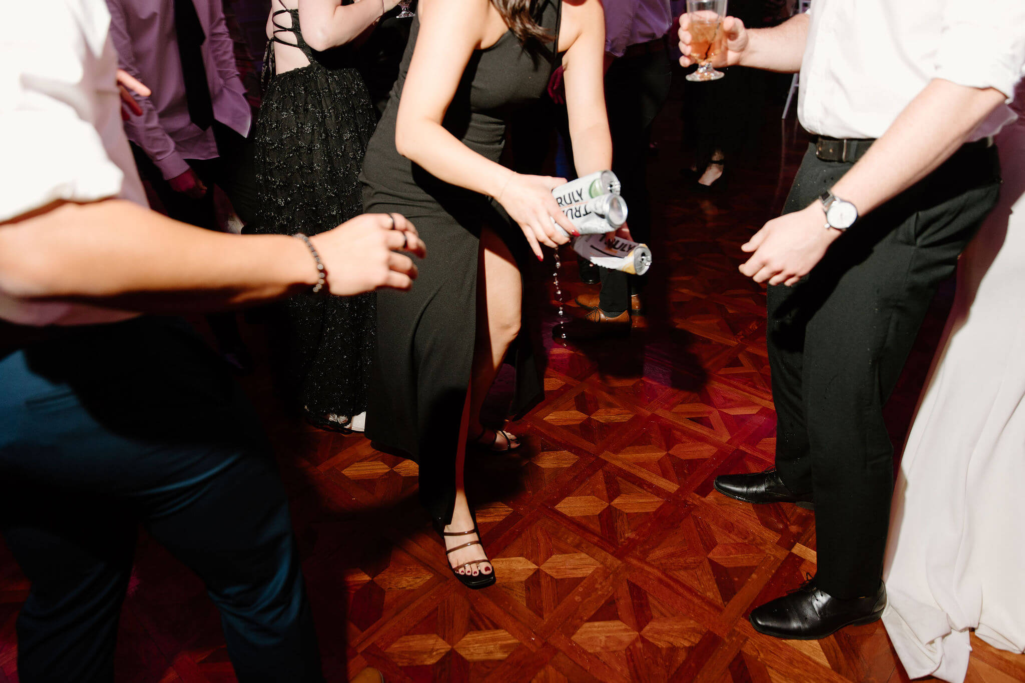 bridesmaid carrying three dripping truly seltzers away from the dance floor