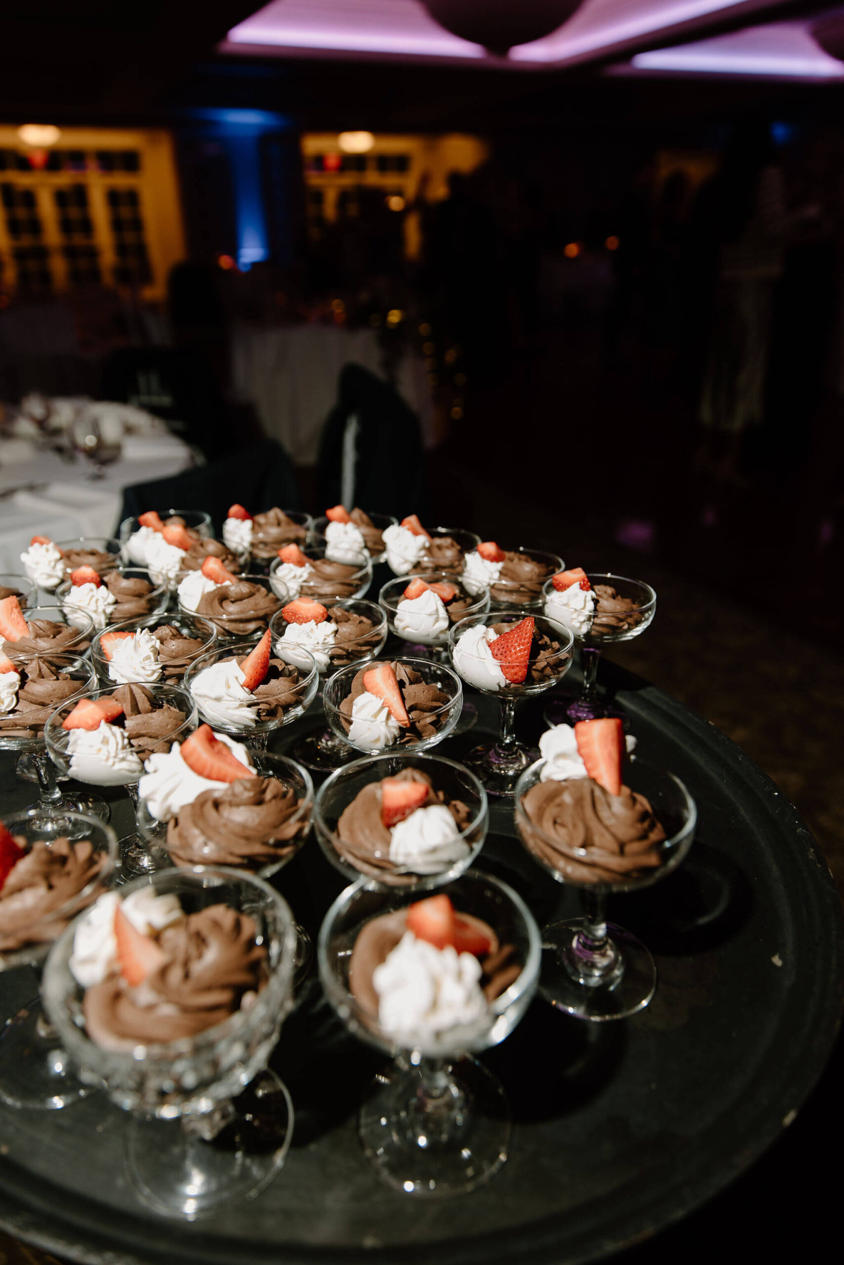 a serving tray filled with chocolate pudding desserts, garnished with whipped cream and a strawberry, at a wedding reception
