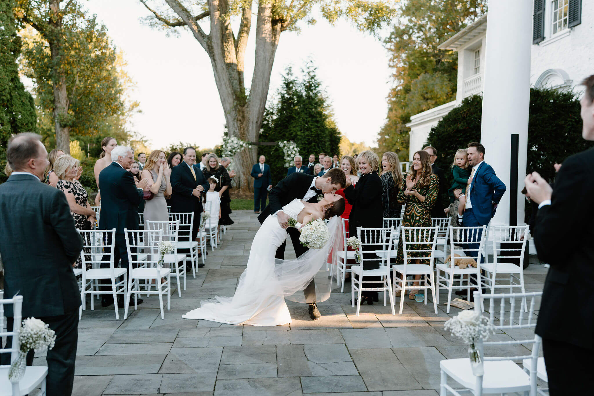 groom dipping his bride during their recessional, guests cheering from their seats