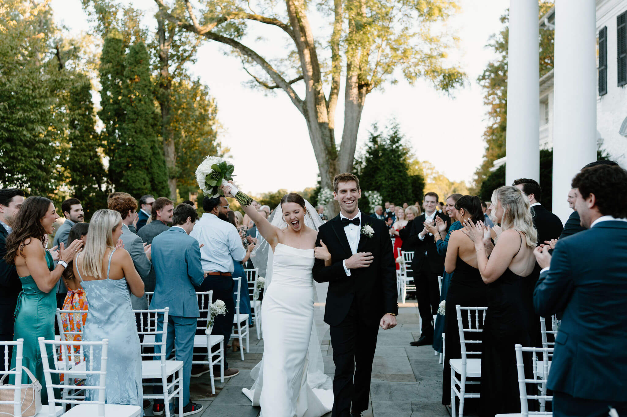 bride and groom smiling and cheering as they exit their wedding ceremony, bride waving her bouquet above her head
