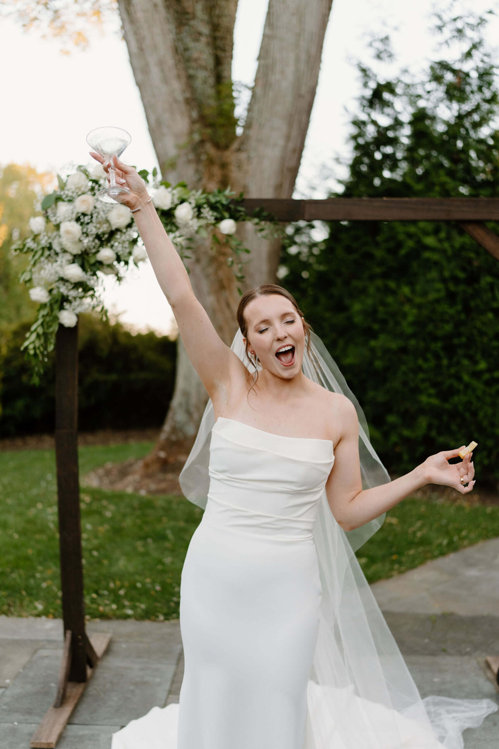 bride smiling with her eyes closed, holding a lemon slice in one hand and an empty martini glass high above her head in the other