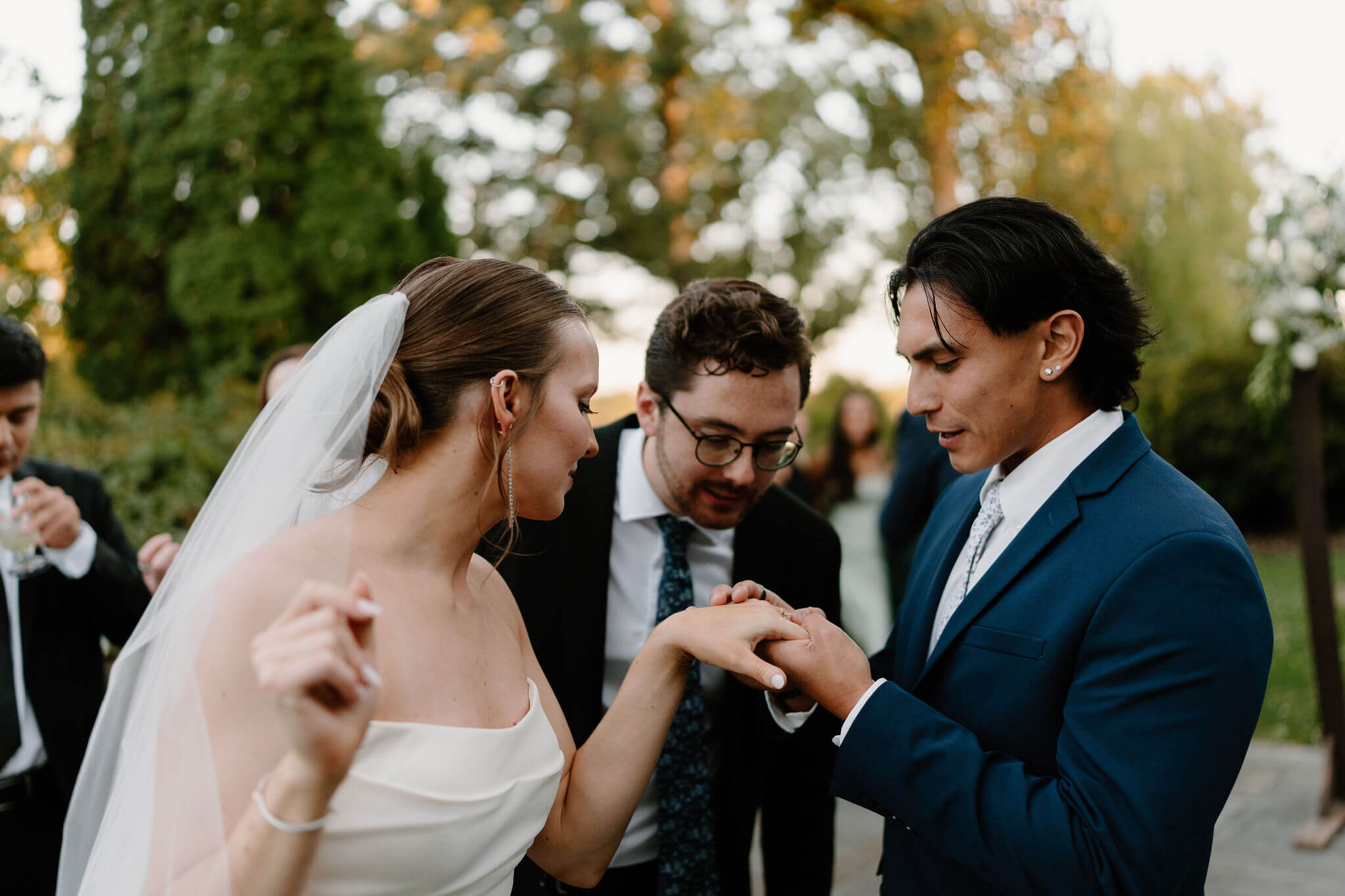 two male guests in suits admiring bride's wedding band and engagement ring as she holds it up for them to see