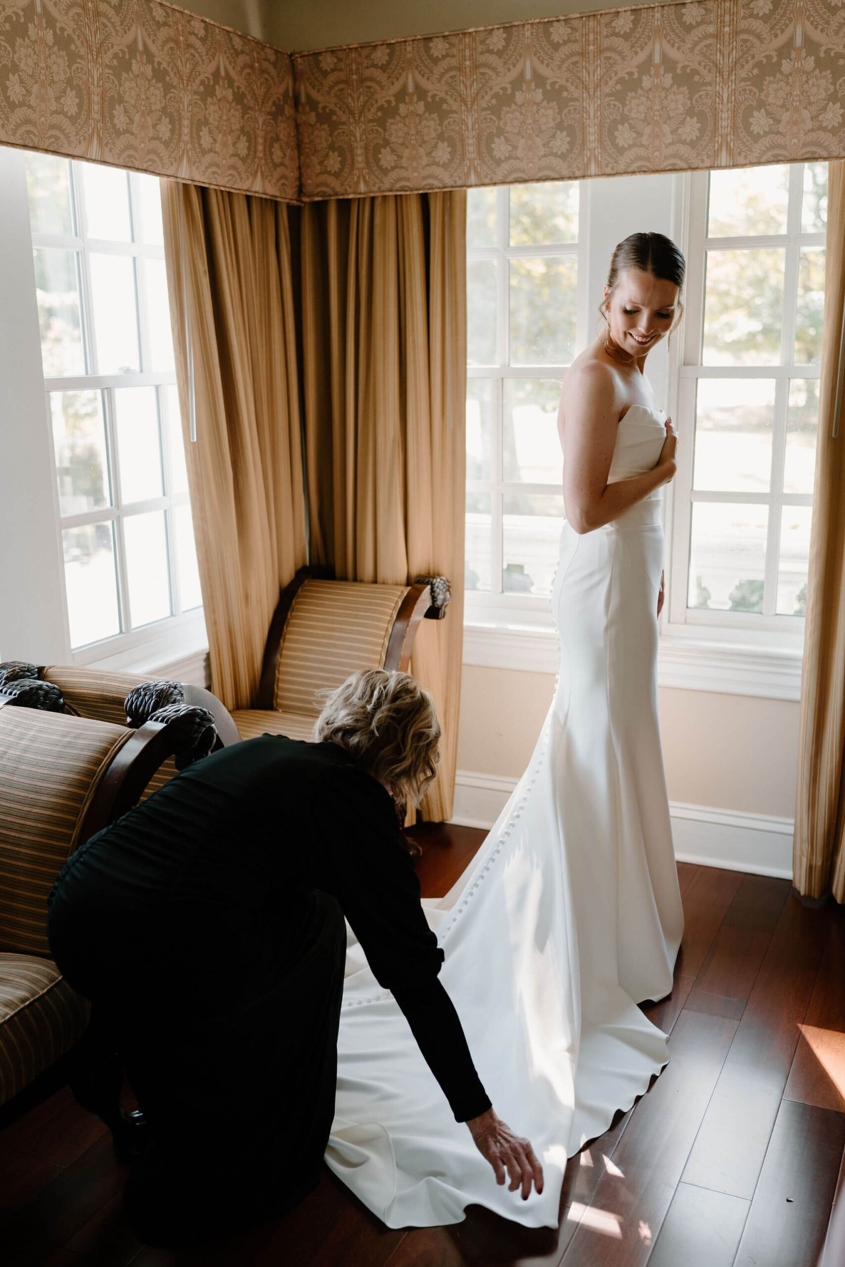 bride's mother (black dress) straightening the train of the bride's wedding gown while she gets dressed