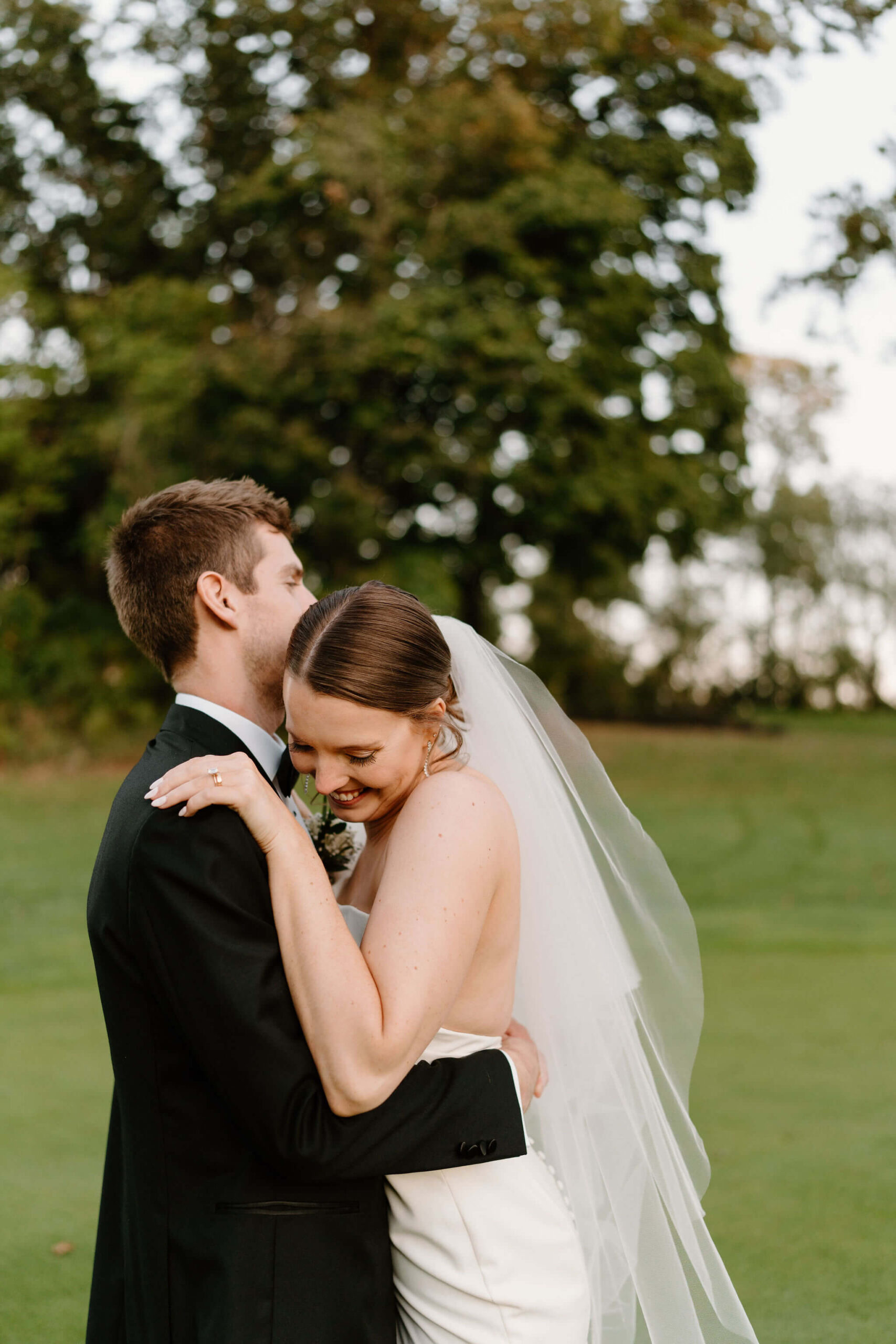 bride laughing into groom's shoulder as they embrace