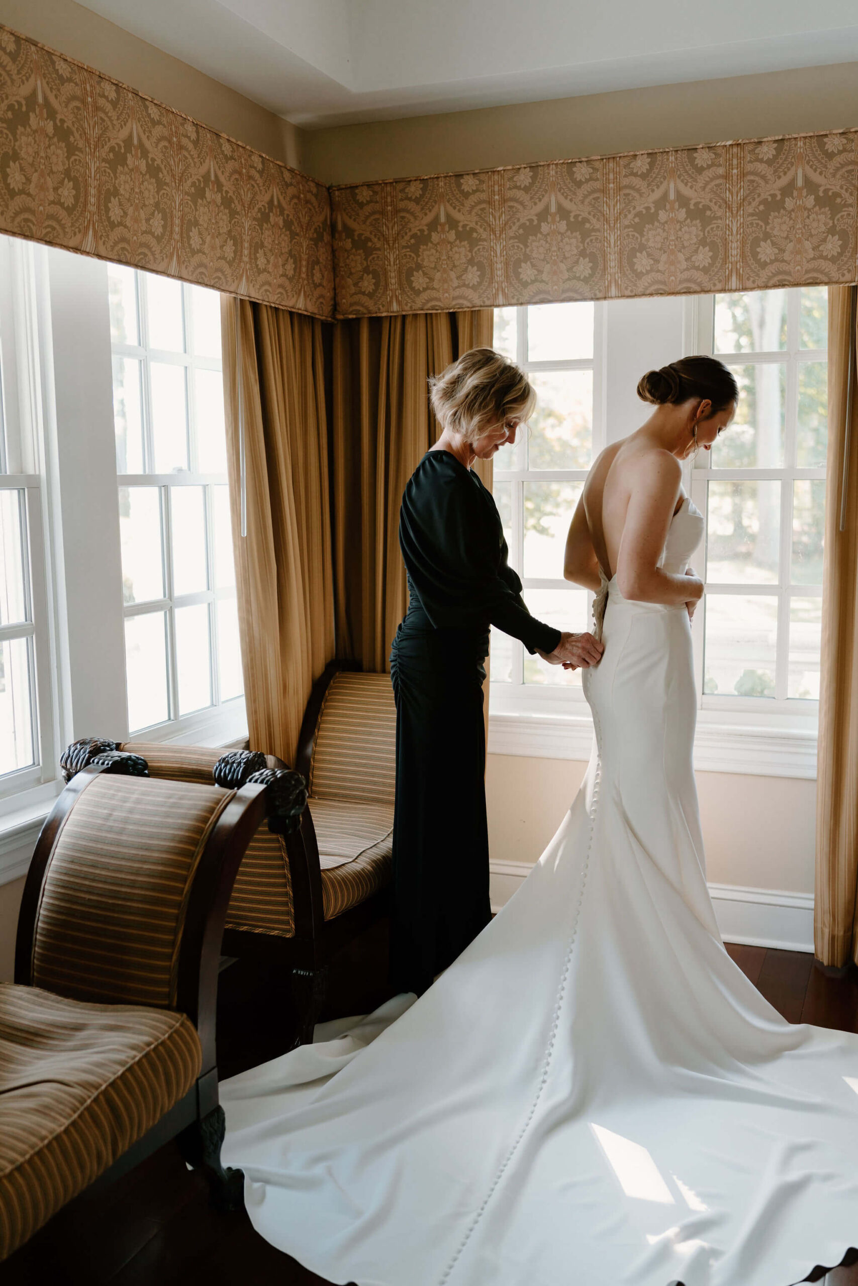 the mother of the bride (black dress) helping the bride into her wedding gown