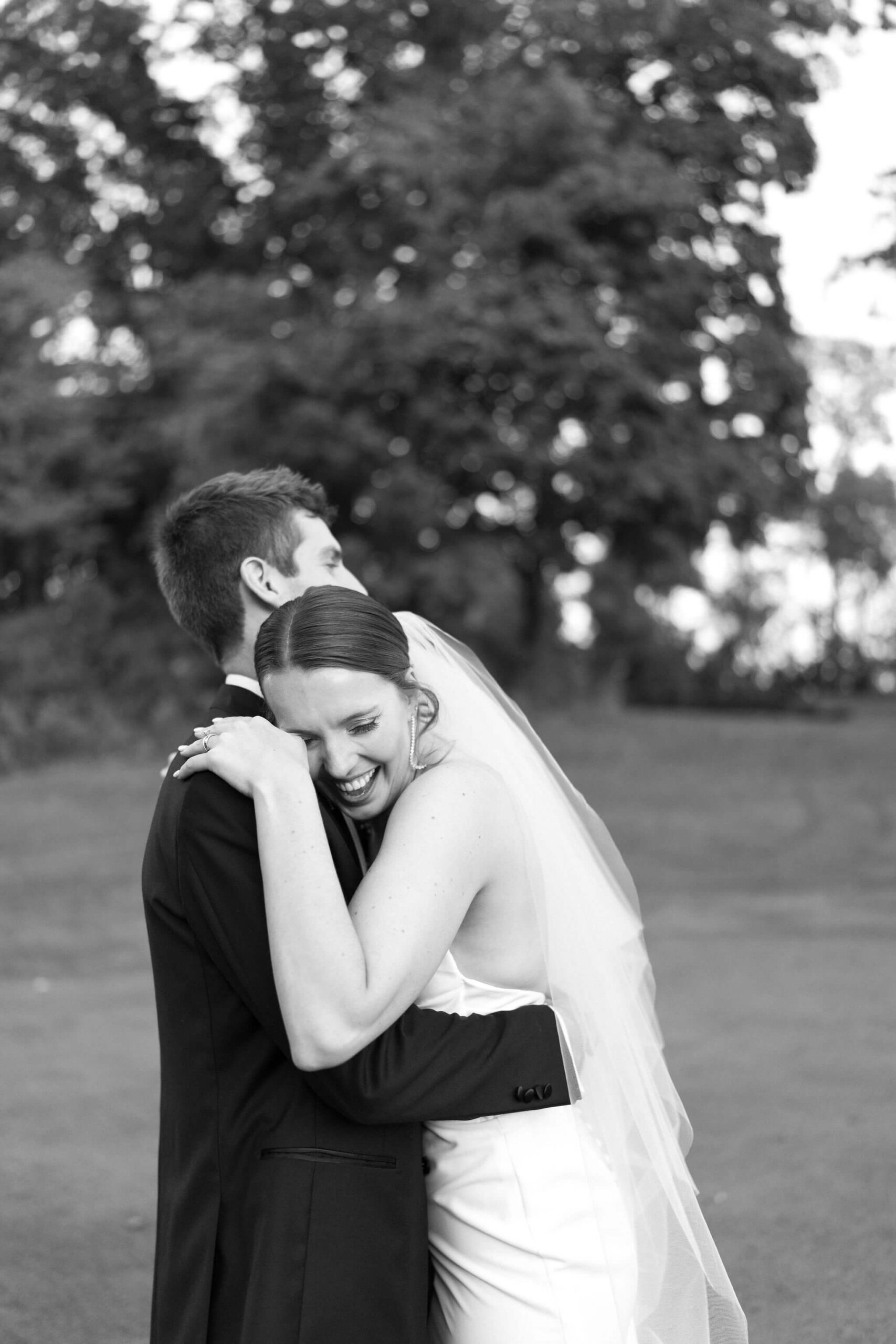 black and white image of bride laughing into groom's shoulder as they hold each other