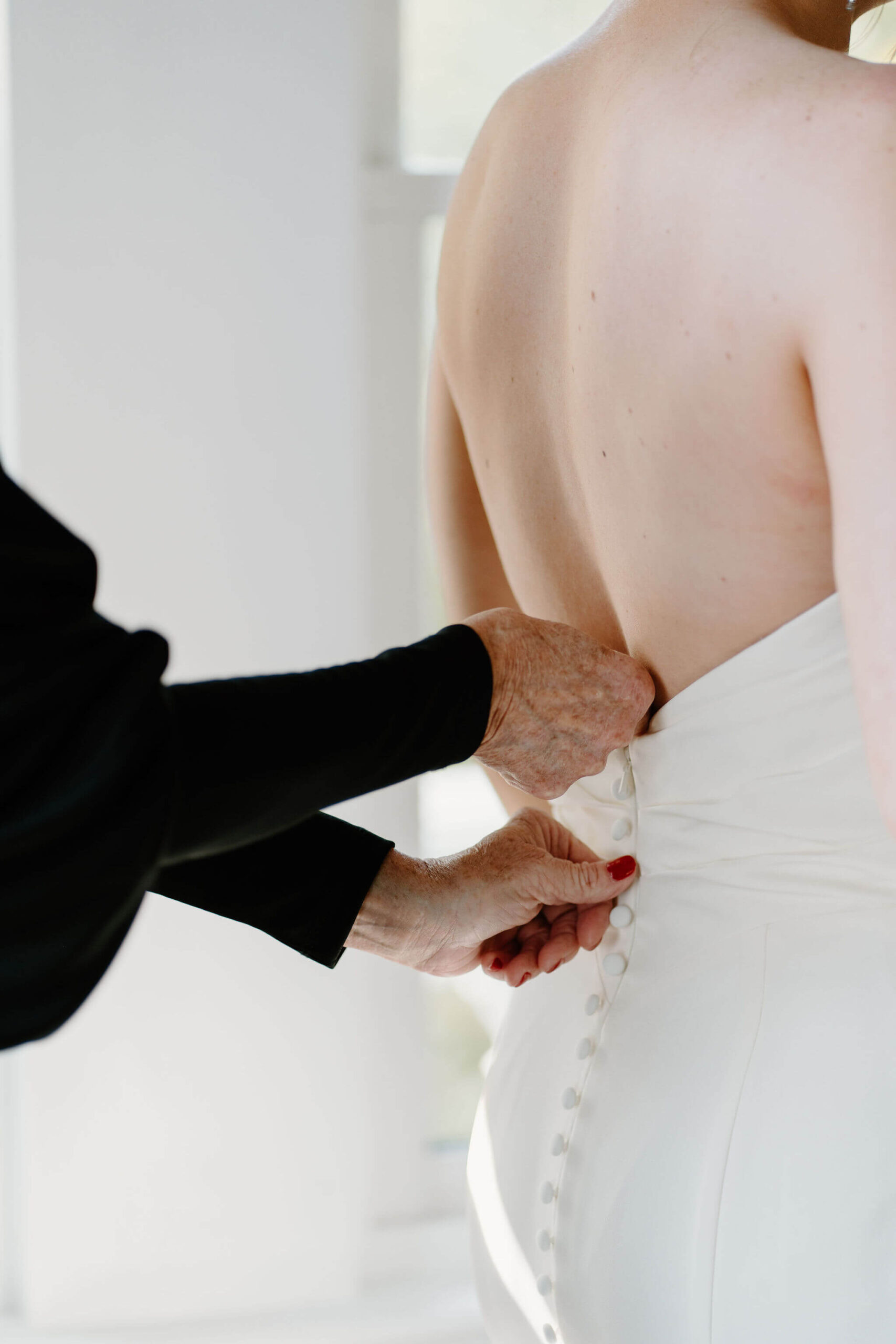 close up of the mother of the bride's hands buttoning the bride's wedding gown