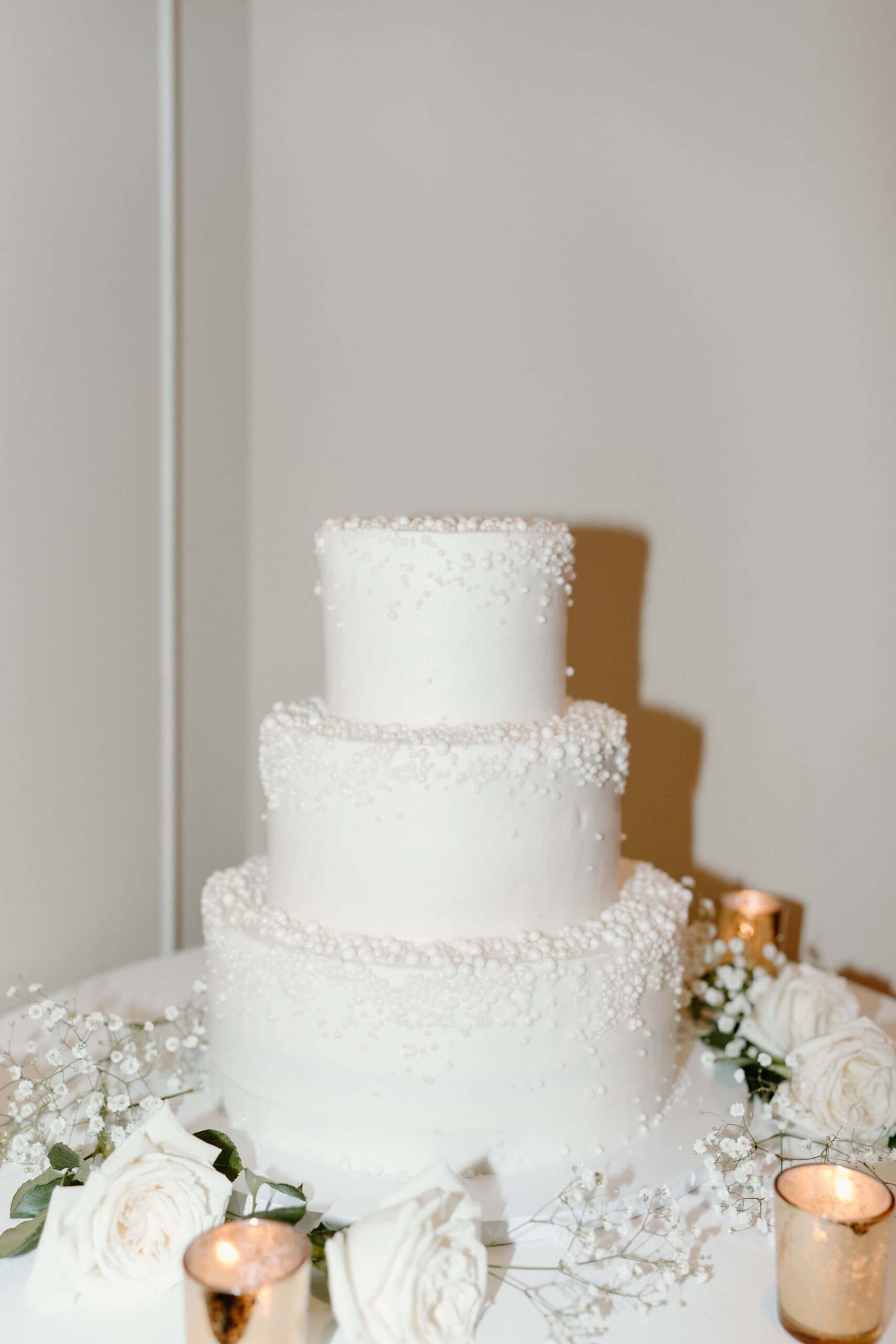 three tiered white wedding cake with pearls of icing on each layer