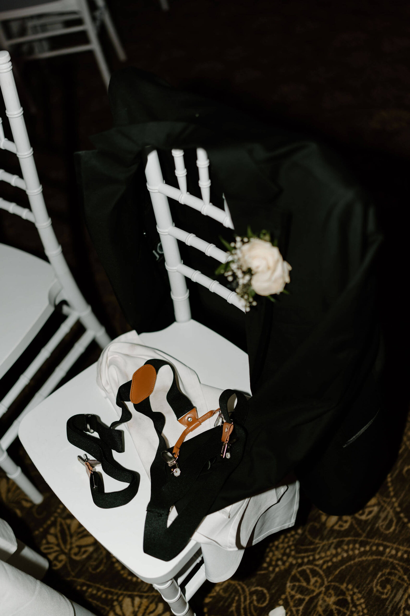 groom's jacket, suspenders, and vest discarded on a white chair during a wedding reception