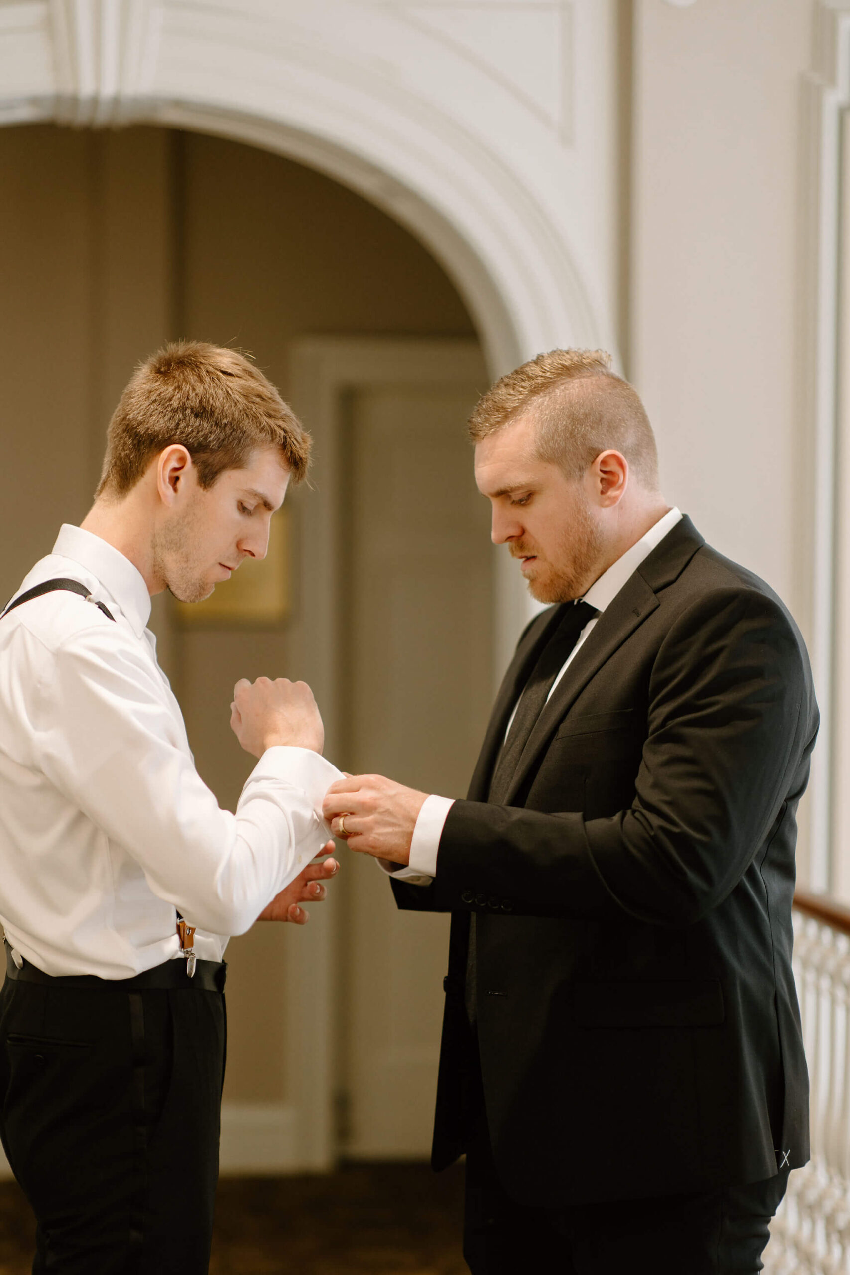 groom's brother (black suit jacket) helping groom (white button down shirt) place his cuff links