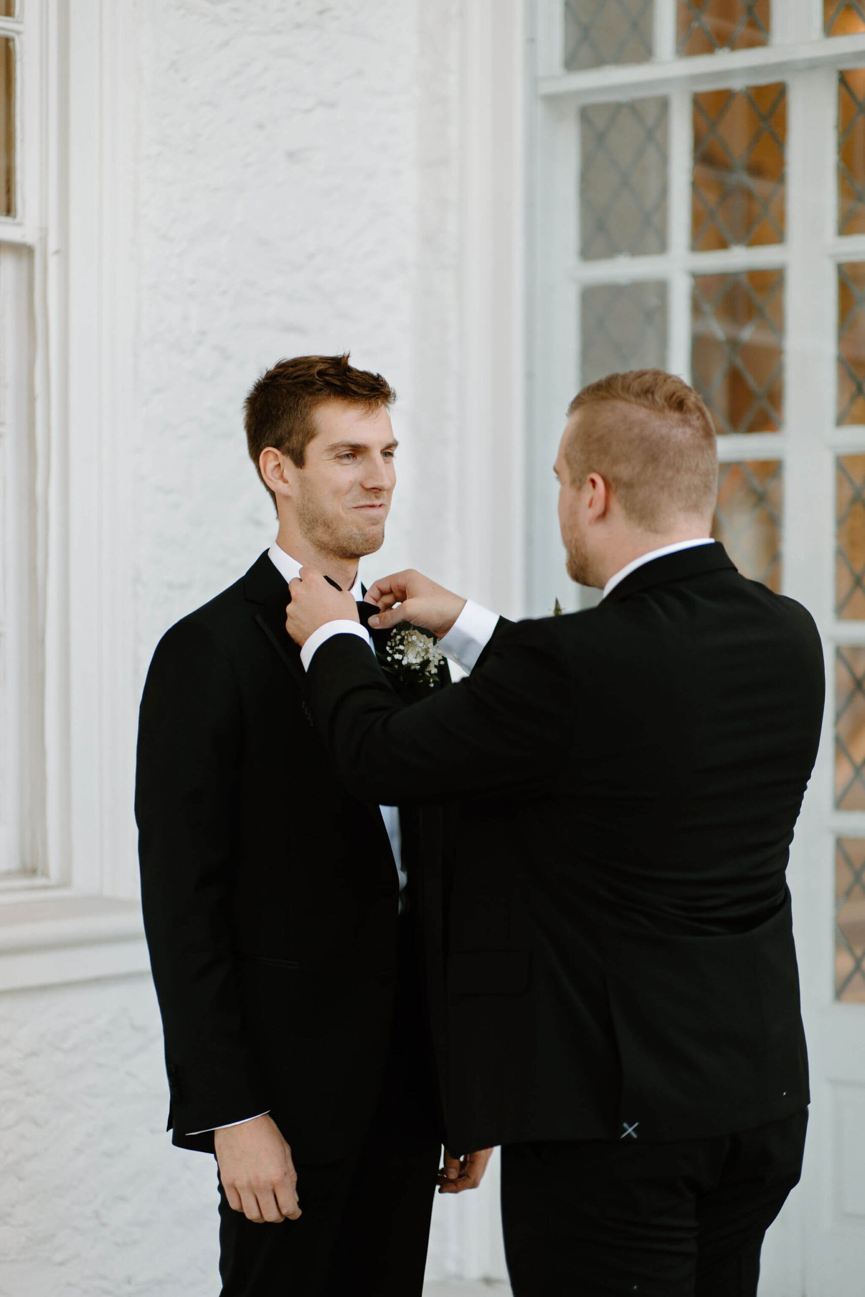groom's brother helping to fix the groom's bow tie, while groom smiles