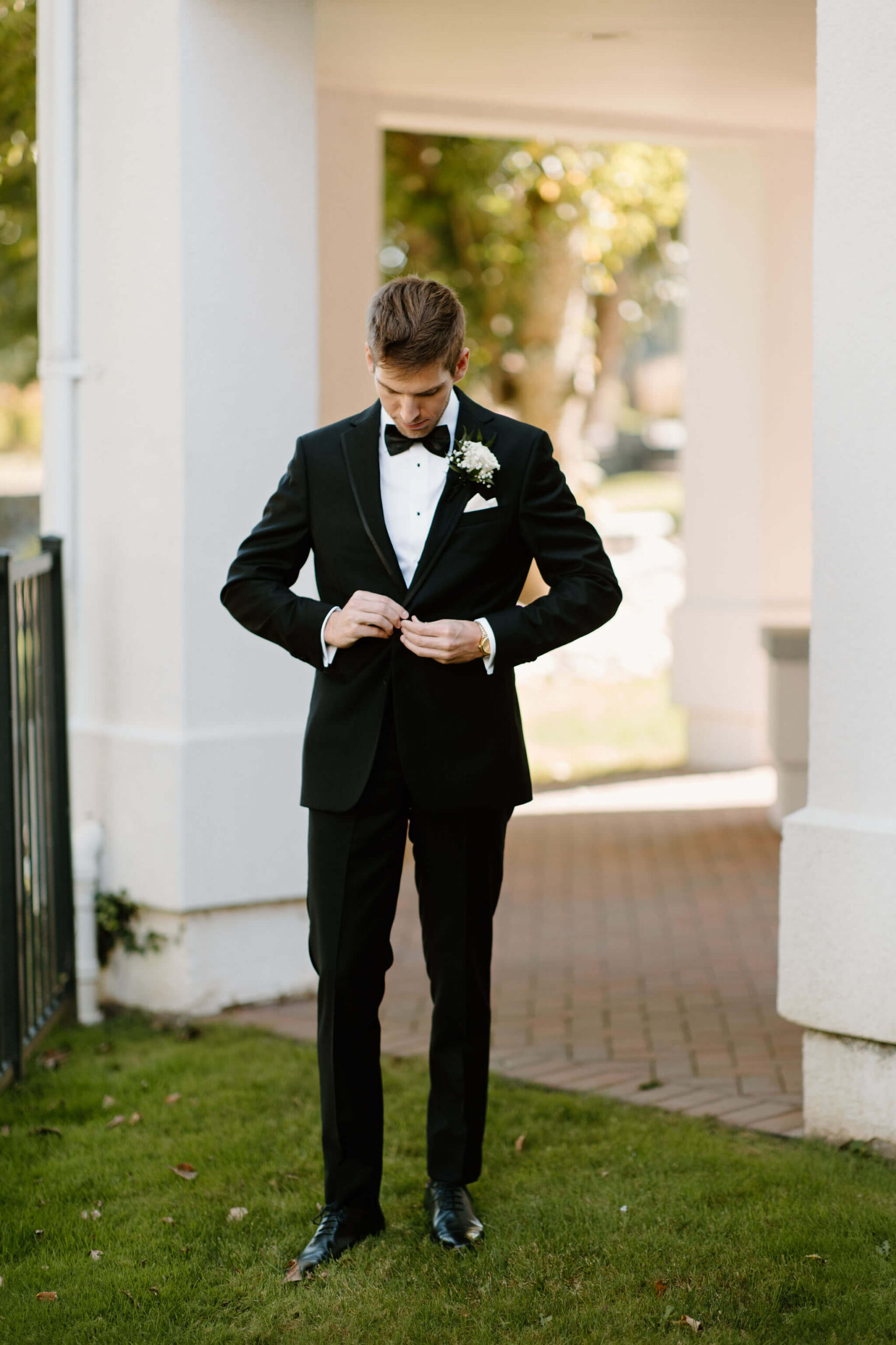 groom in a black suit looking down while buttoning his jacker