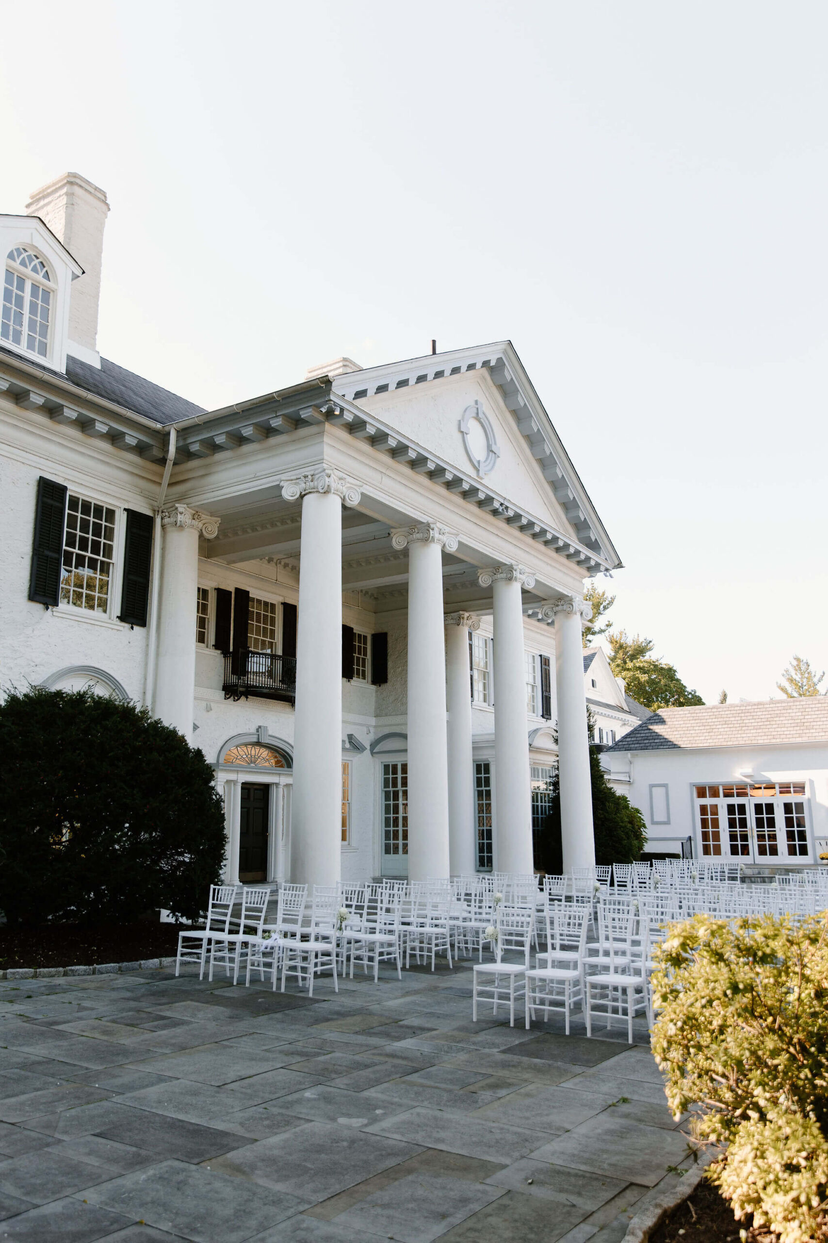 Ceremony site of Radnor Valley Country Club in Philadelphia, PA, with white chairs set up on a stone patio in front of a large white columned building