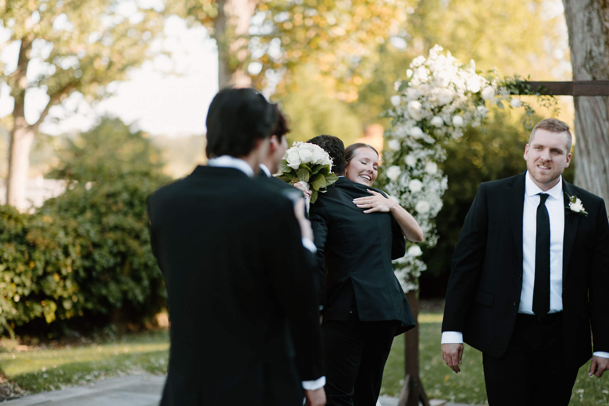 bride hugging one of the groomsmen, with two other groomsmen in the foreground