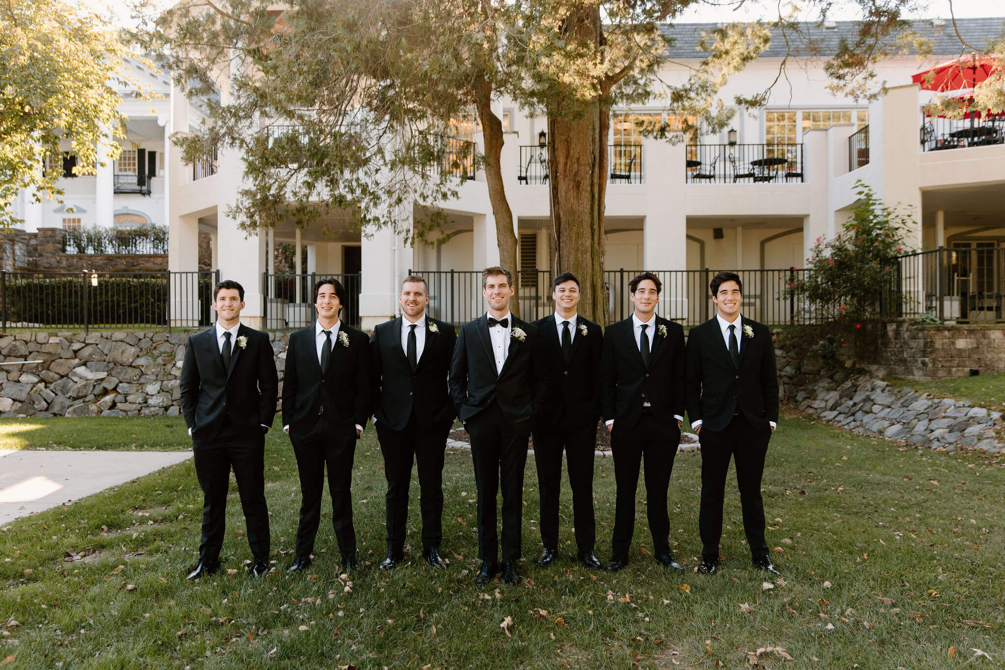 Groomsmen standing in a line with their hands in their pockets, all wearing black suits
