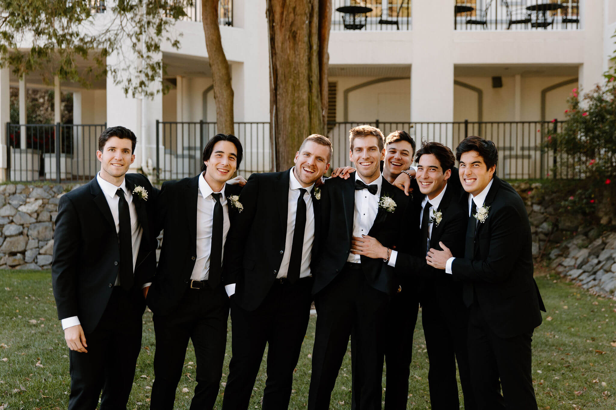 groom and groomsmen all in black suits smiling at the camera with their arms around each other