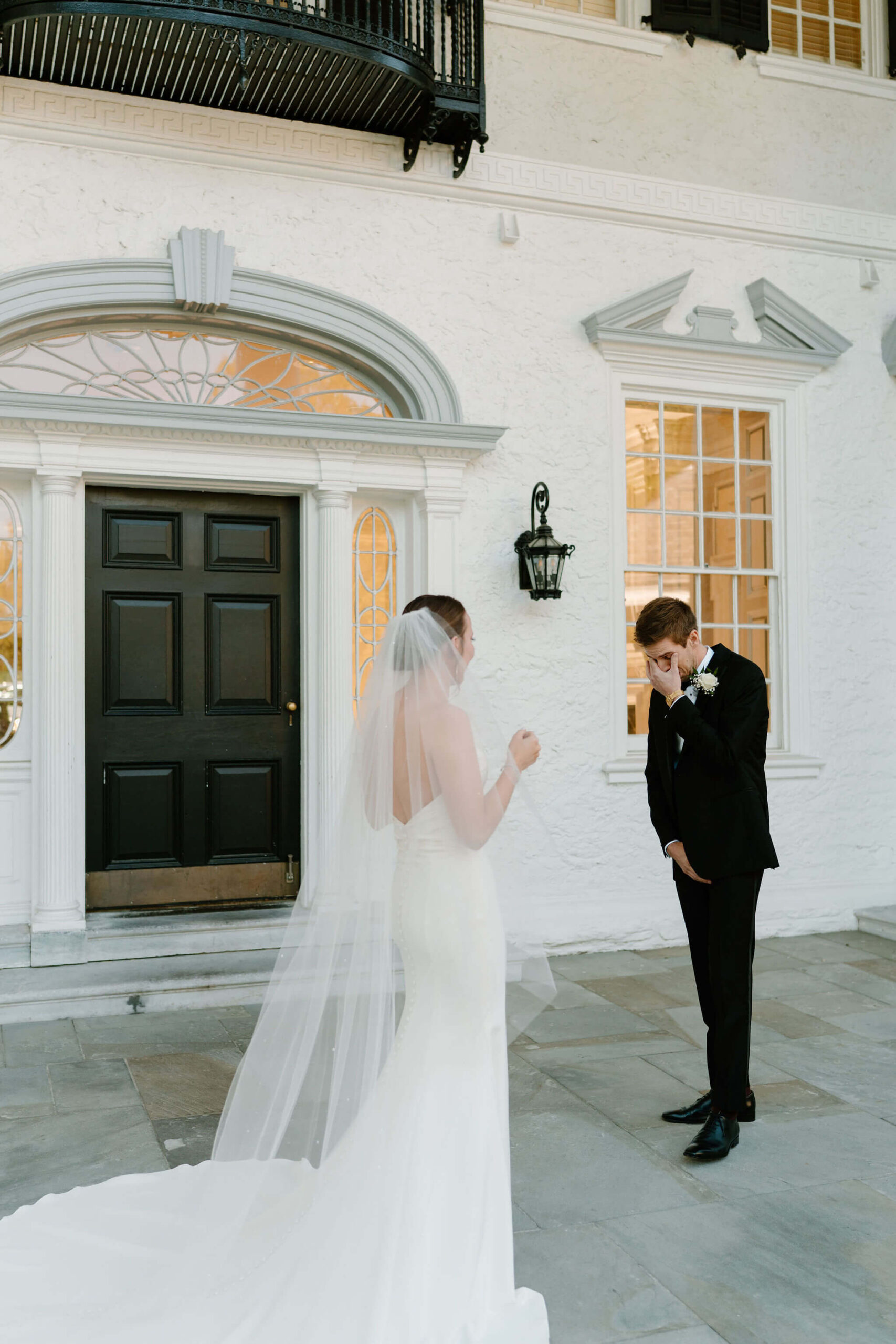 Groom with his hand covering his eyes, crying, during his first look with his bride on their wedding day