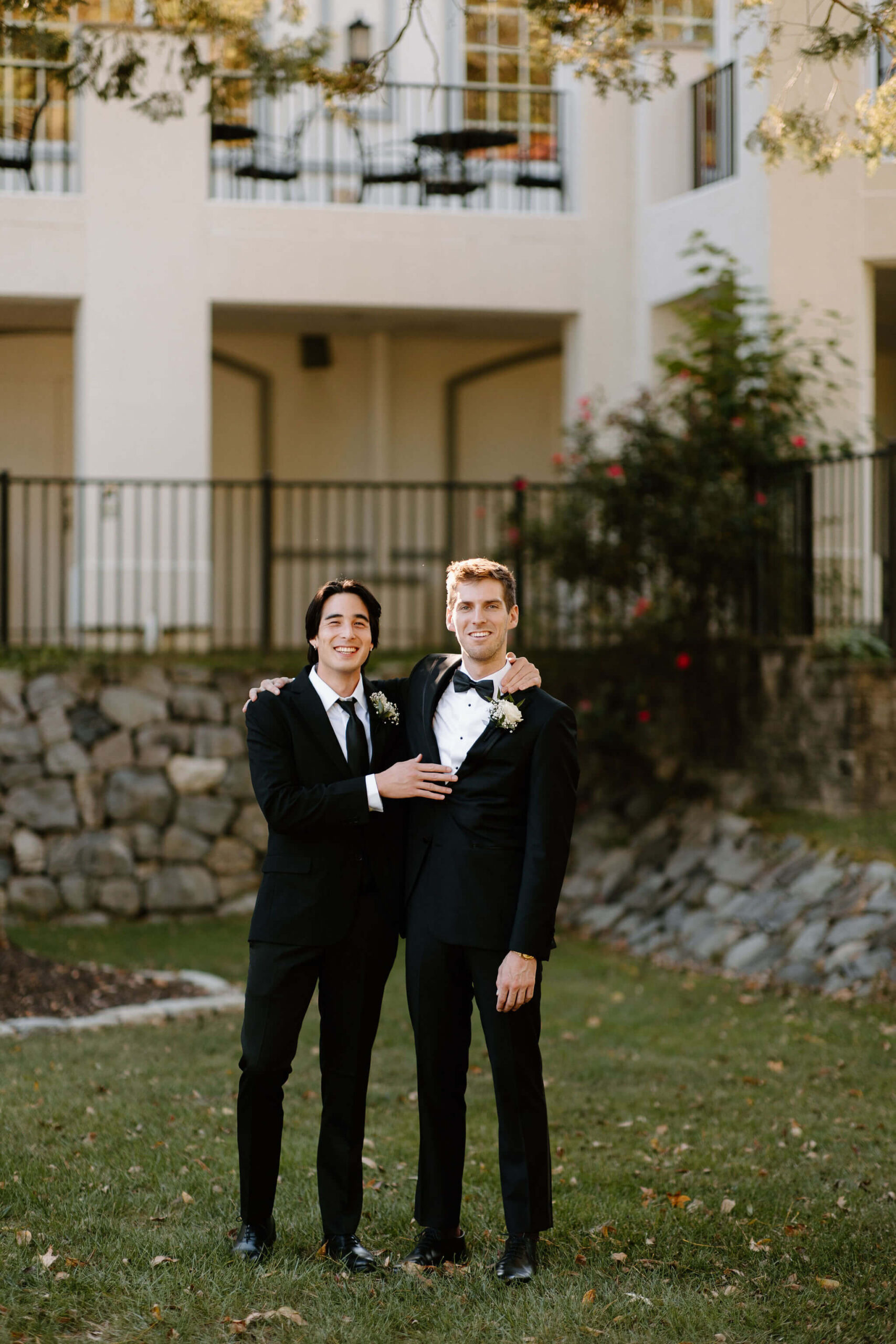 Groom and his groomsmen, both wearing black suits, smiling at the camera with an arm around each other