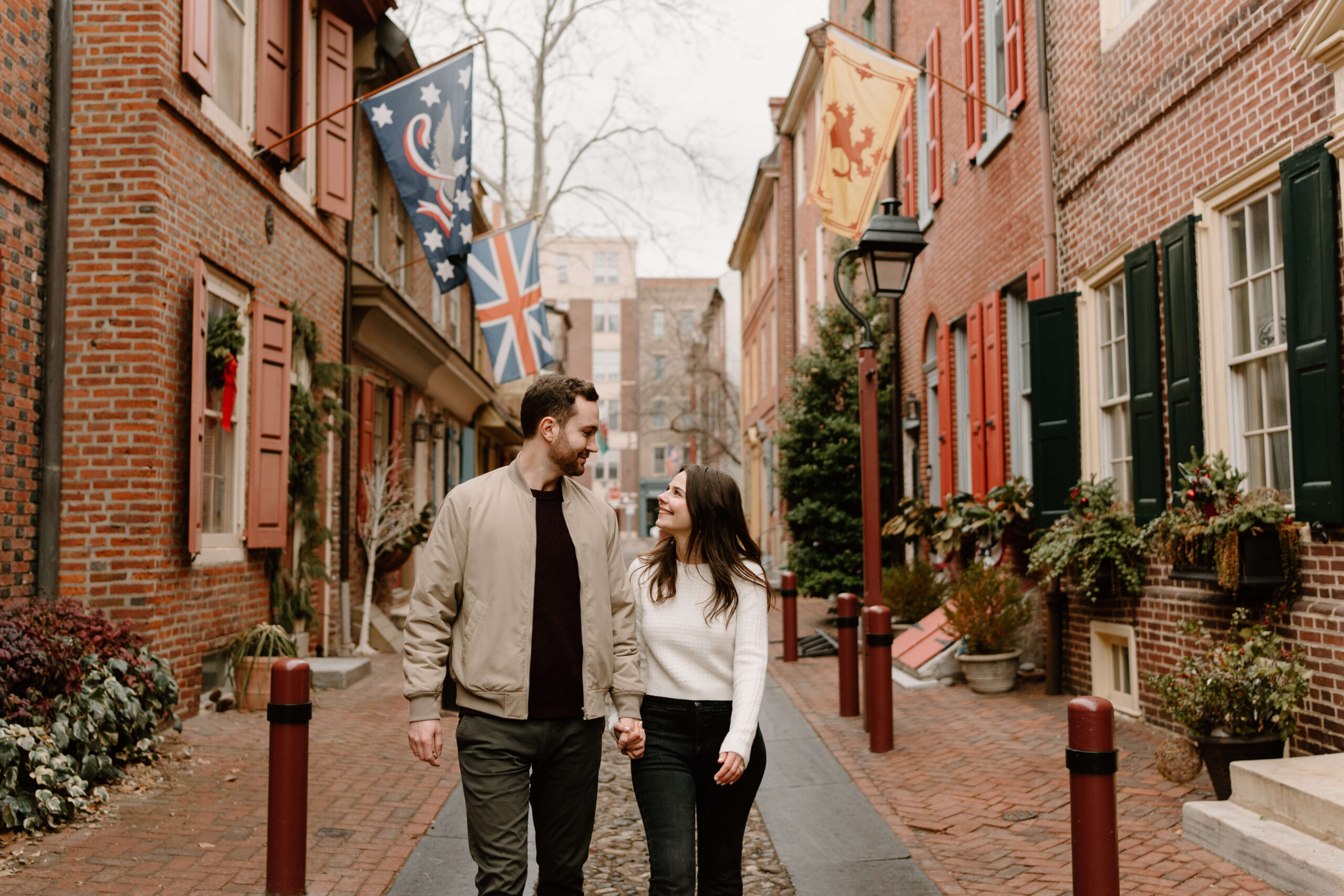 a couple holding hands and walking, smiling at each other, on the cobblestone streets of Elfreth's Alley in Philadelphia