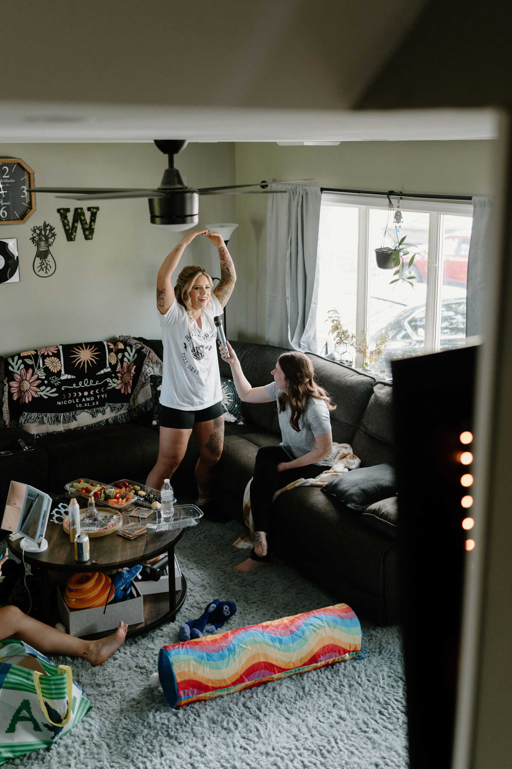 bride singing karaoke in her living room while her bridesmaids sit on the couch and floor and do their hair and makeup