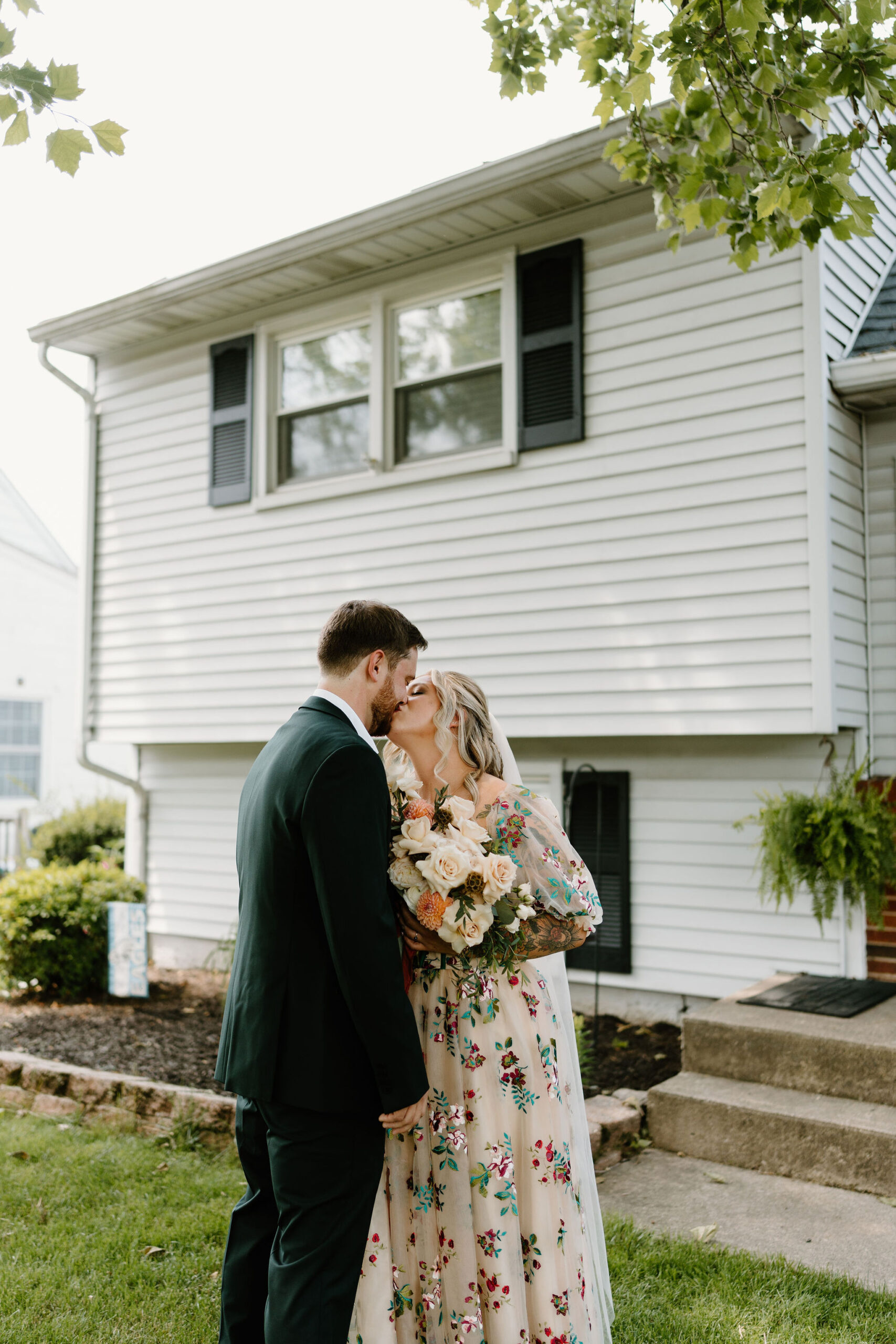 bride in a colorful embroidered wedding dress kissing her groom in a green suit after their first look