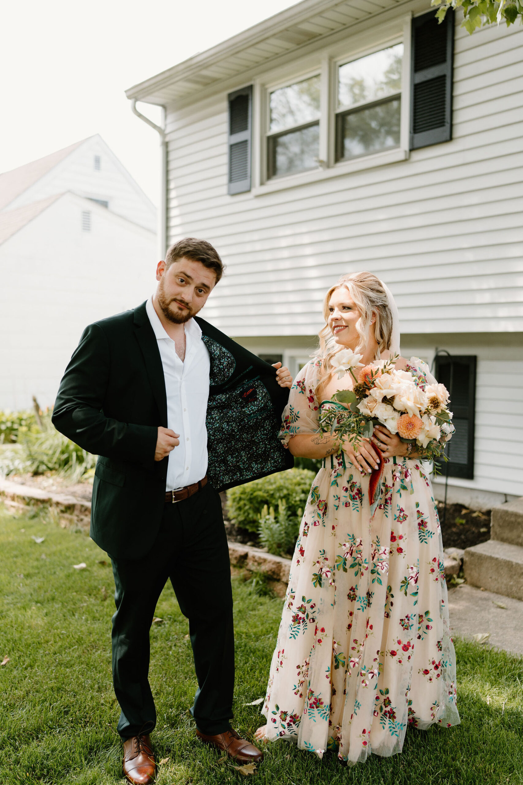 bride in a colorfully embroidered wedding dress smiling at her groom while he shows off the custom lining of his suit jacket to the camera