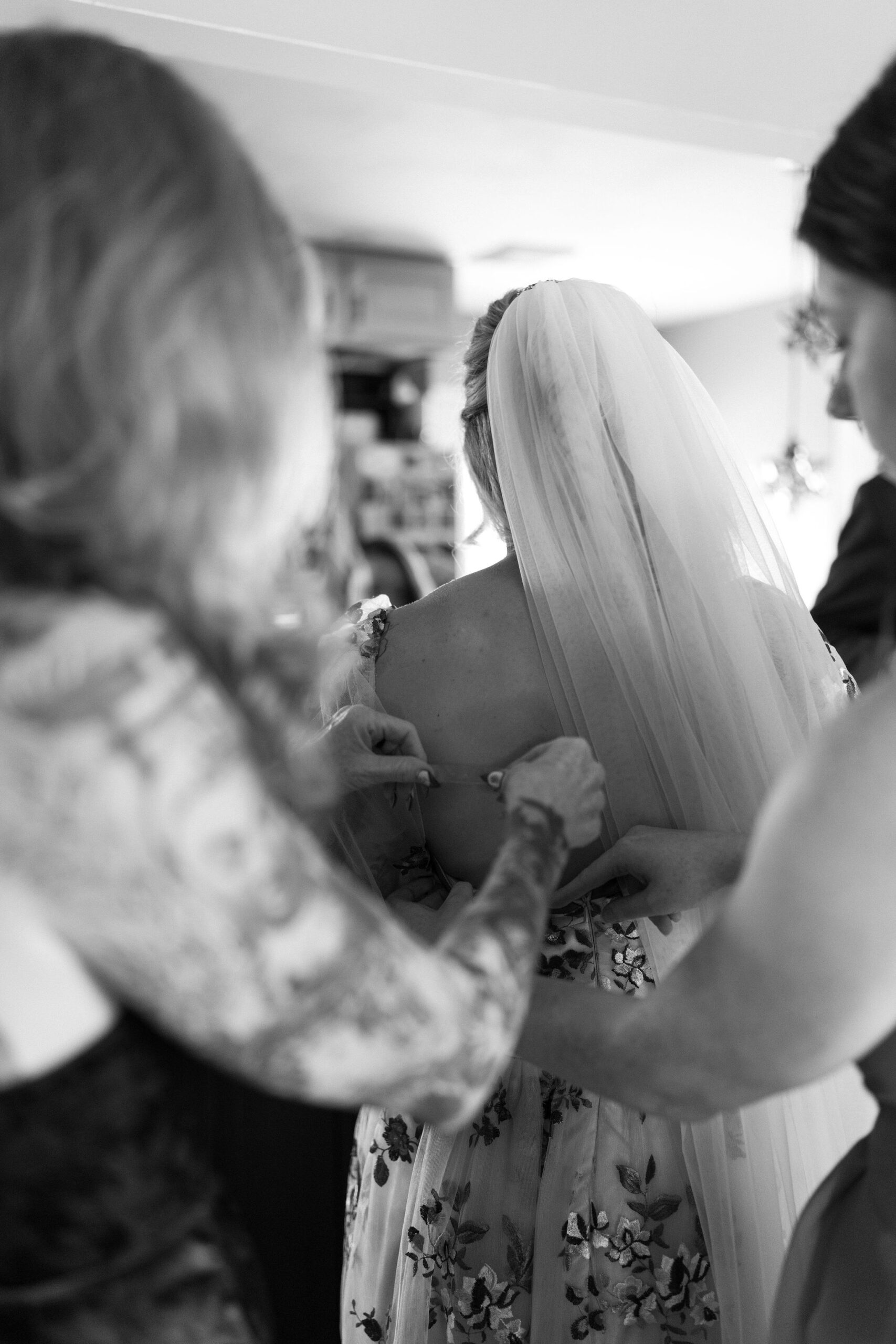 black and white image of bridesmaids helping to tape bride's dress using garment tape