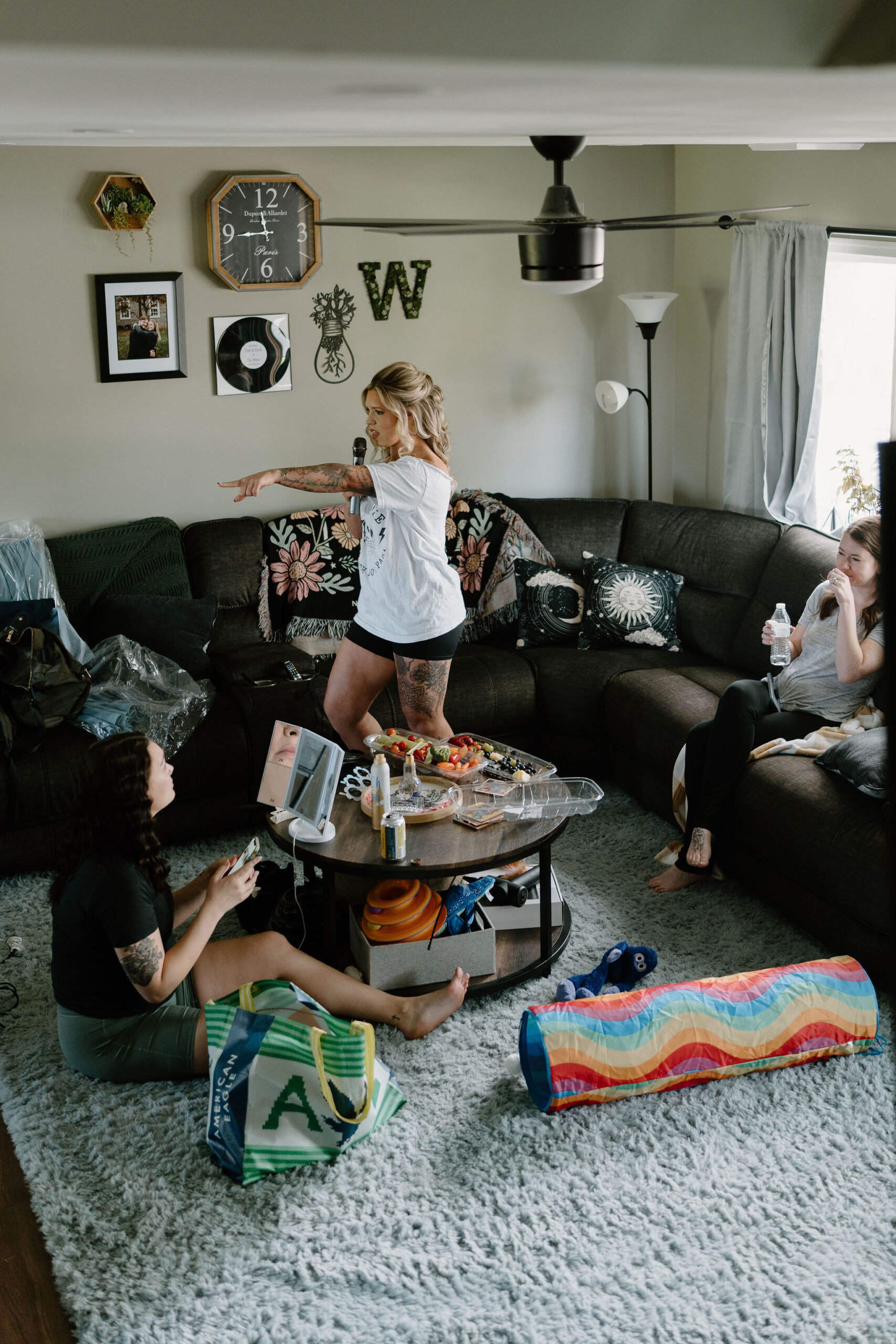 bride singing karaoke in her living room while her bridesmaids sit on the couch and floor and do their hair and makeup