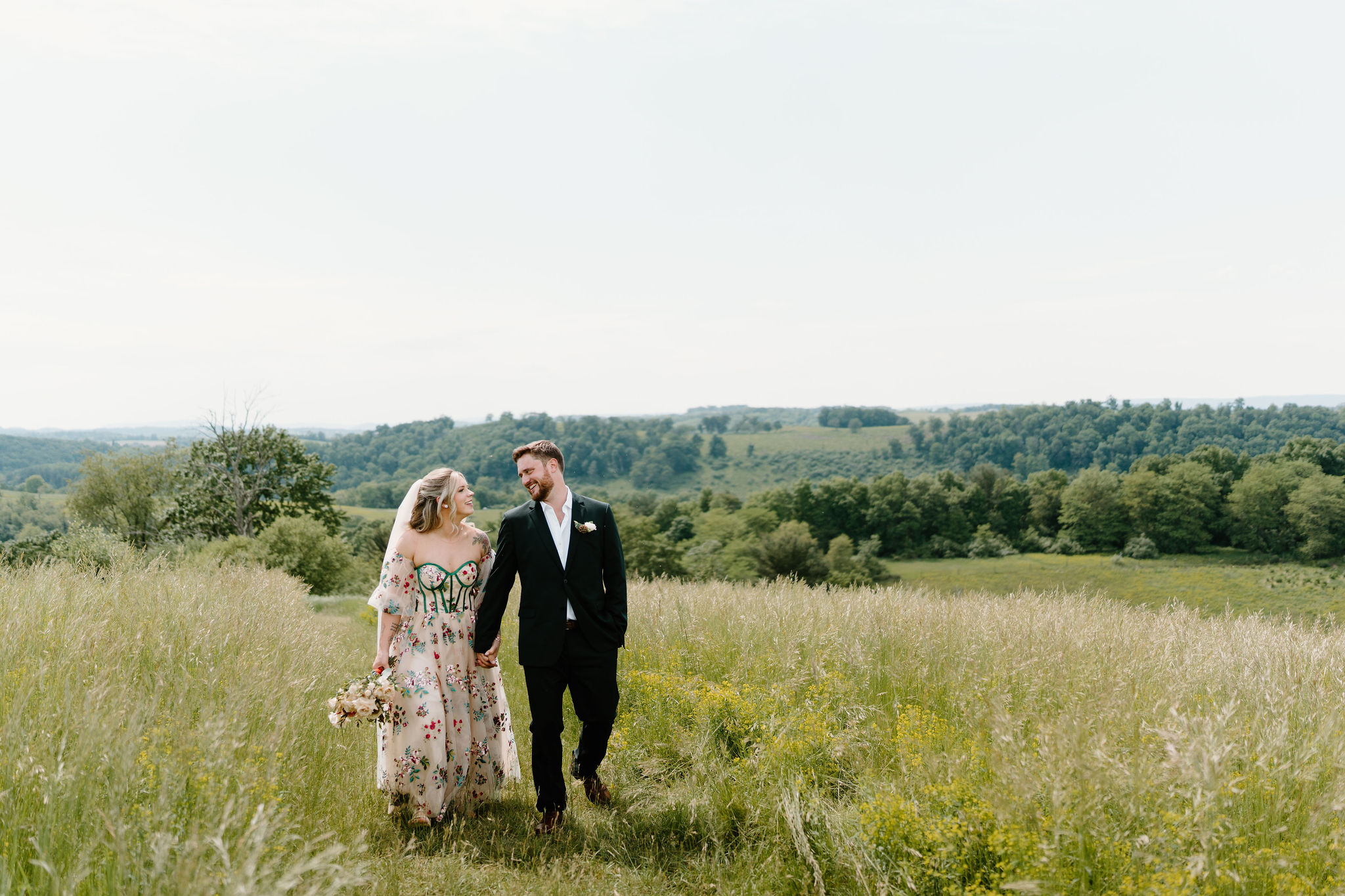 bride and groom holding hands and smiling at each other as they walk through an overgrown grassy field in Lehigh Valley, Pennsylvania