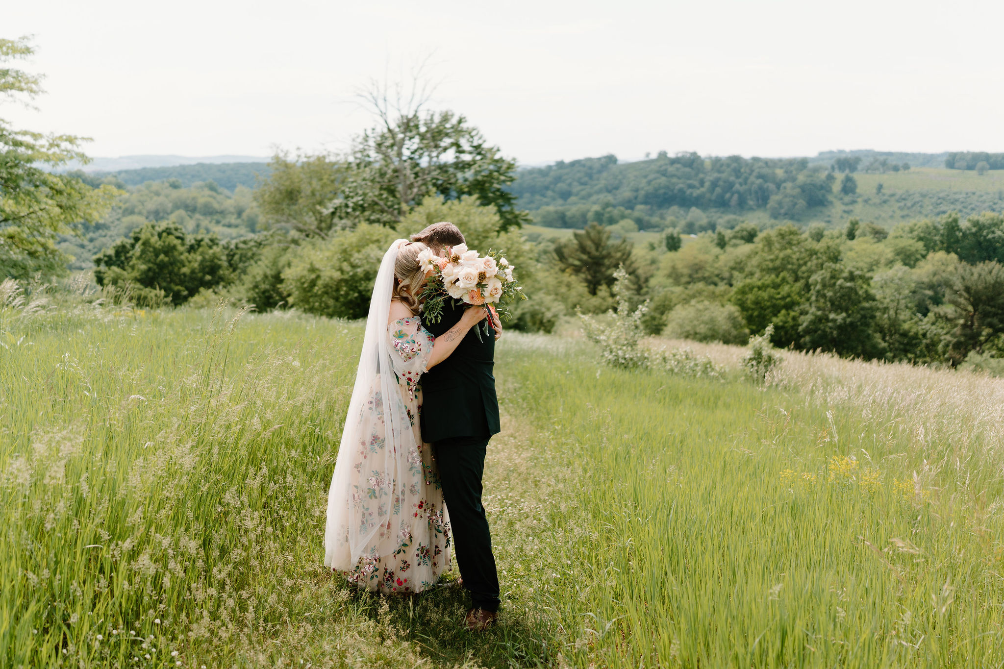 bride and groom embracing on their wedding day in a tall field, her face tucked into his shoulder