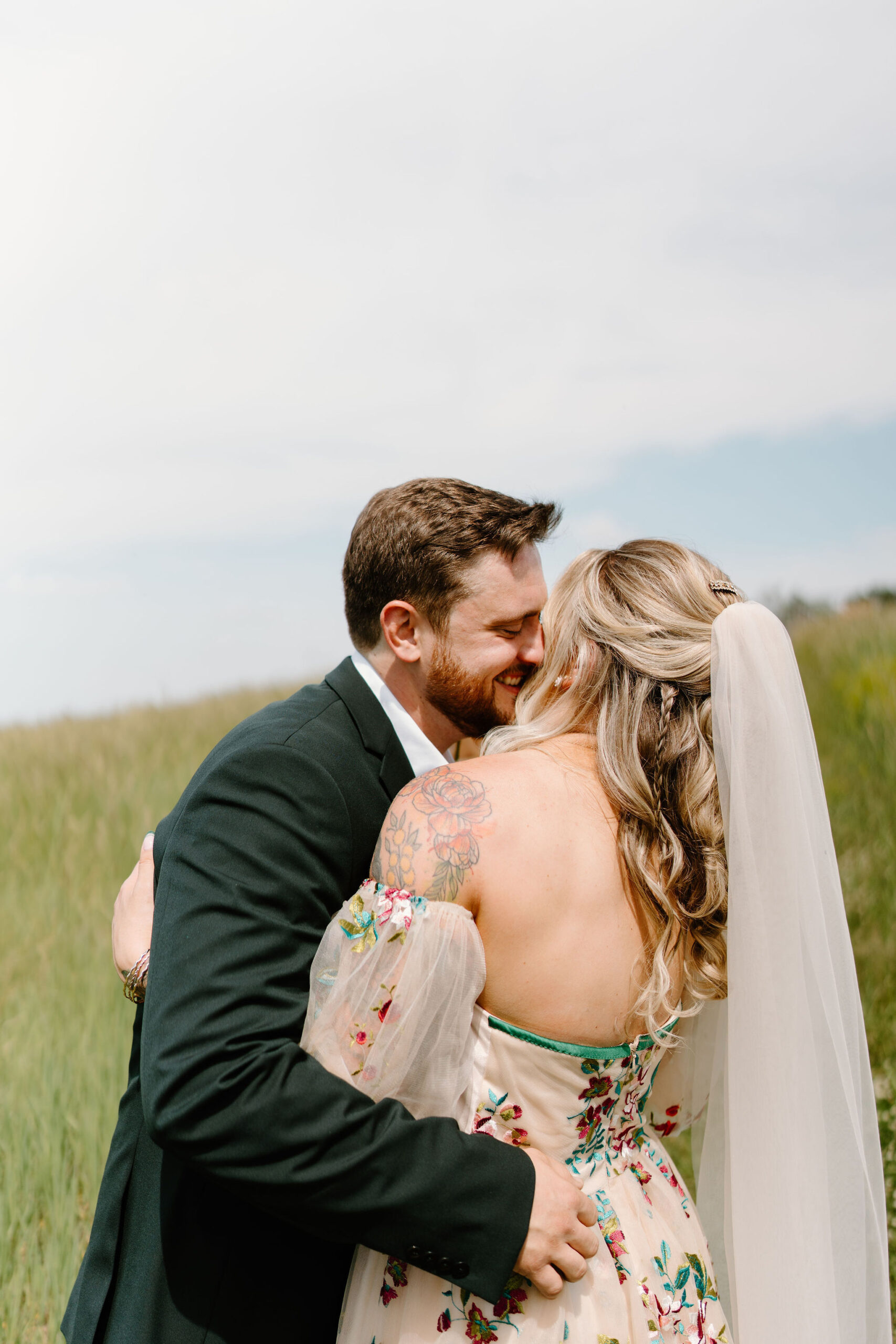 groom (green suit) holding his bride and smiling as they embrace