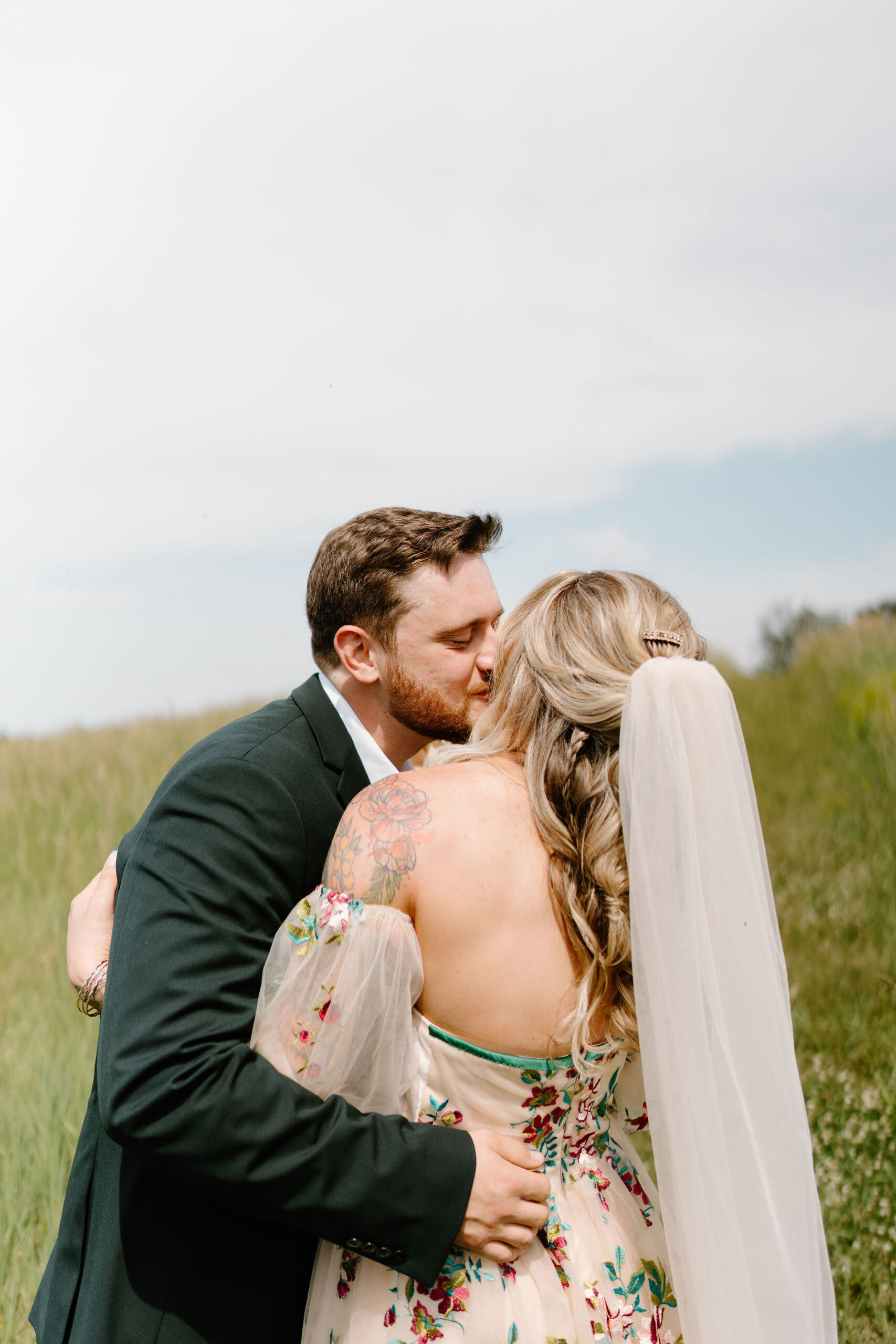 groom holding his bride tight and kissing her on the cheek while she faces away from the camera